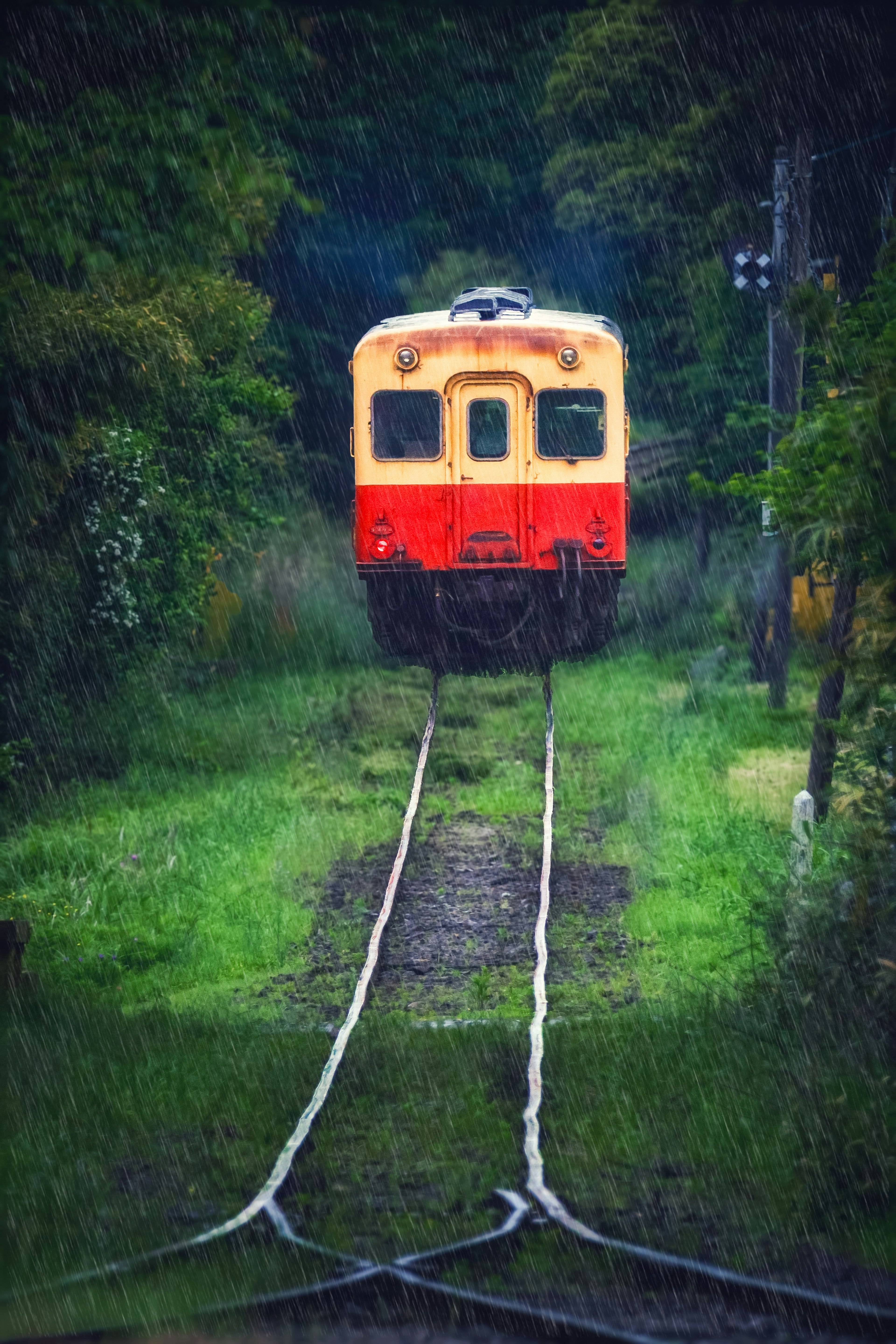 Sebuah kereta merah dan kuning dikelilingi oleh pepohonan di ujung rel