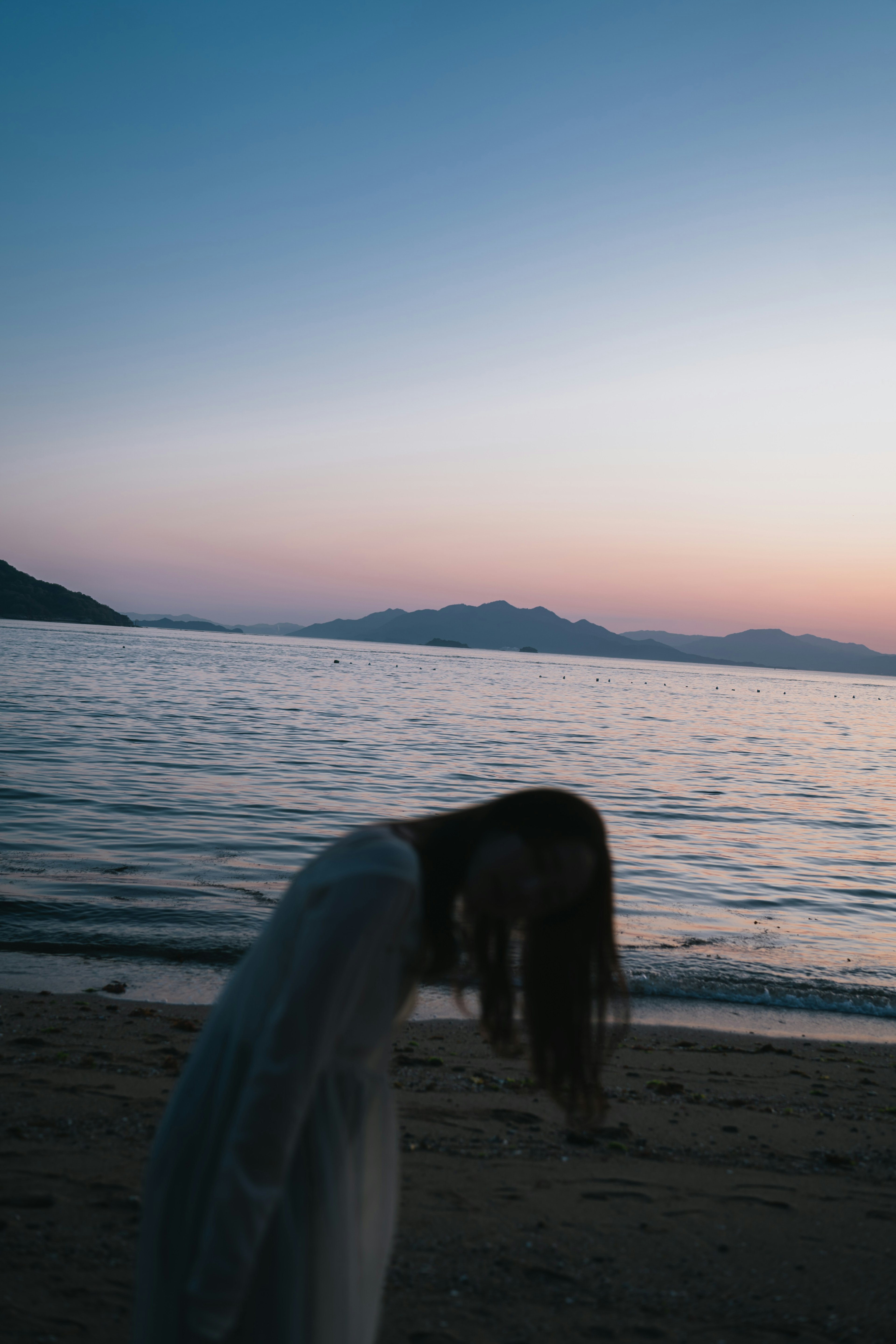 海辺で髪を垂らす白い服の女性夕焼けの空と静かな水面