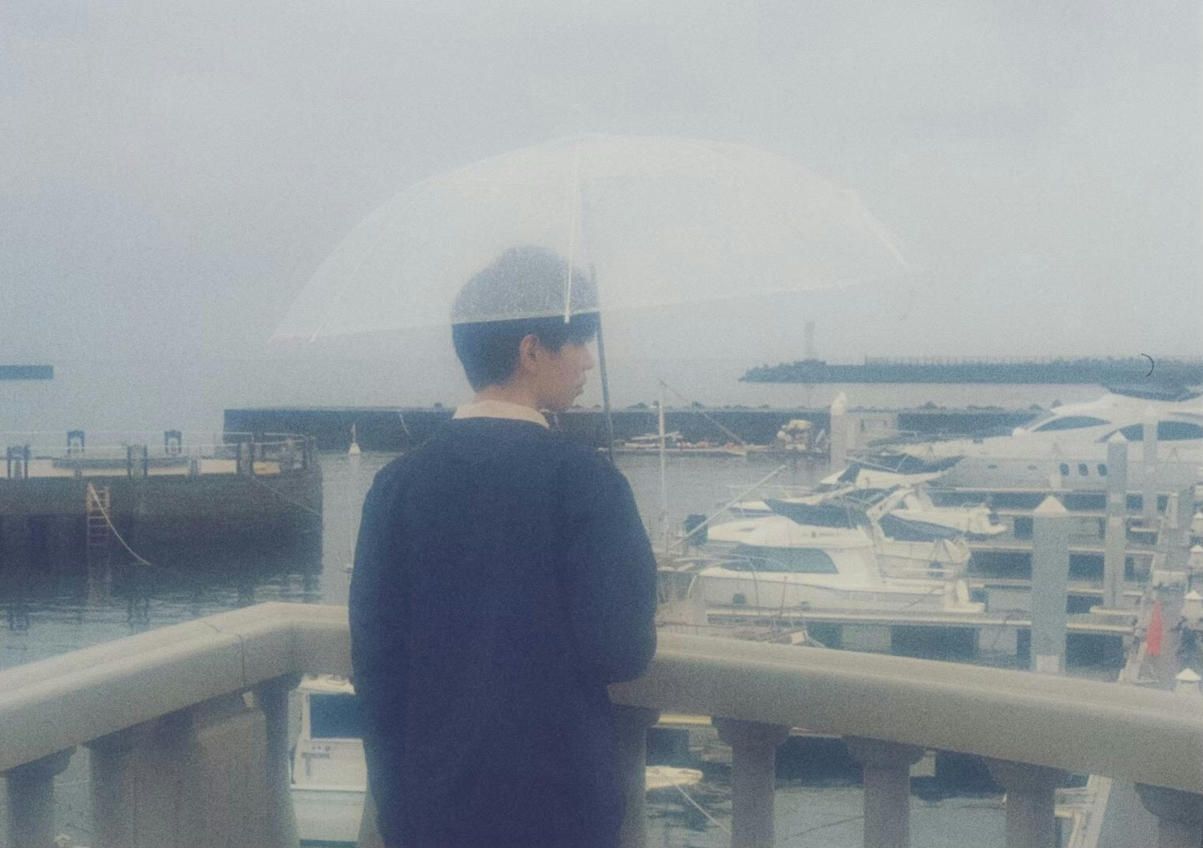 Person mit einem Regenschirm, die Boote am Meer betrachtet