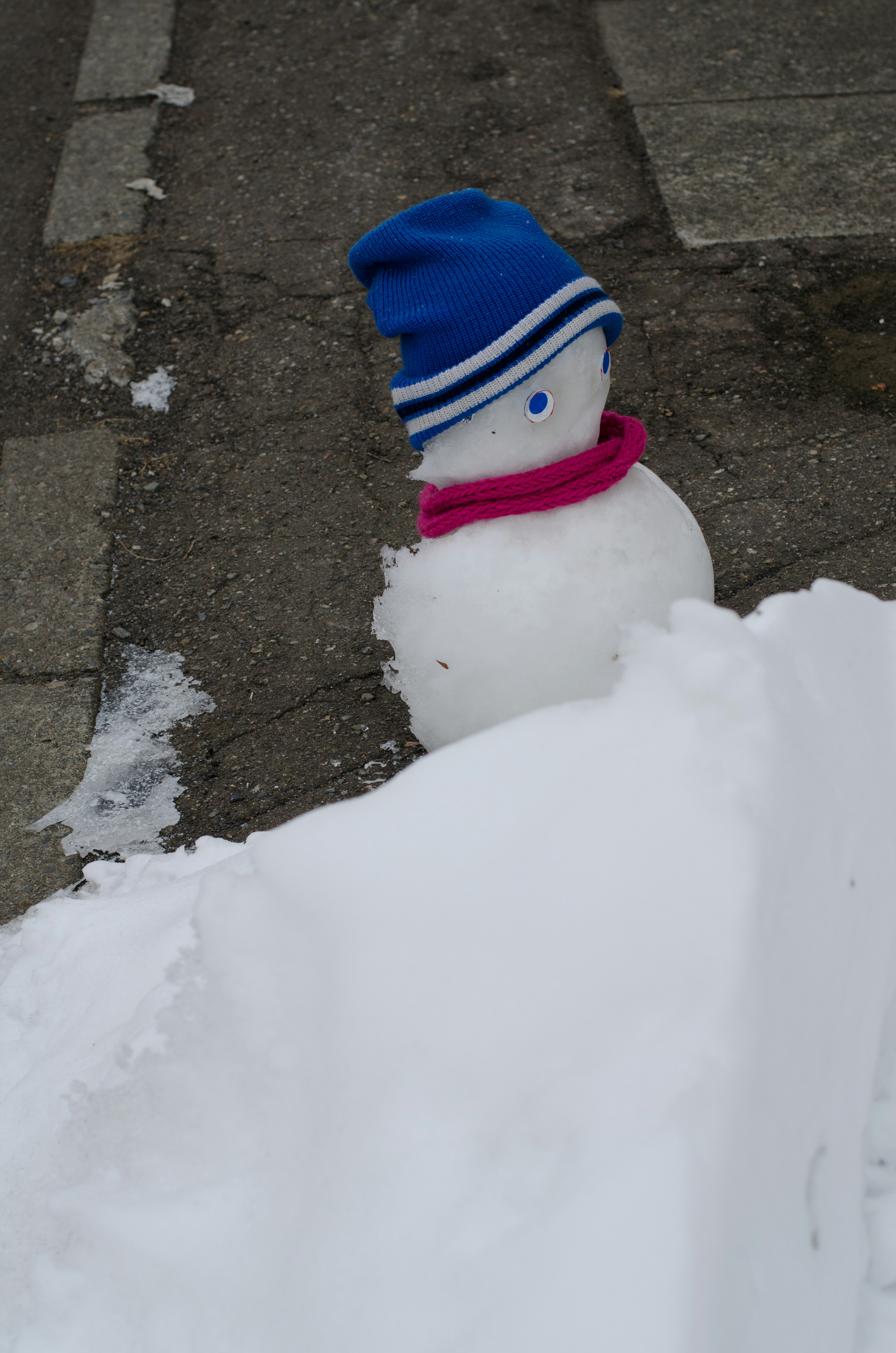 Ein Schneemann mit einem blauen Hut und einem rosa Schal, teilweise im Schnee begraben