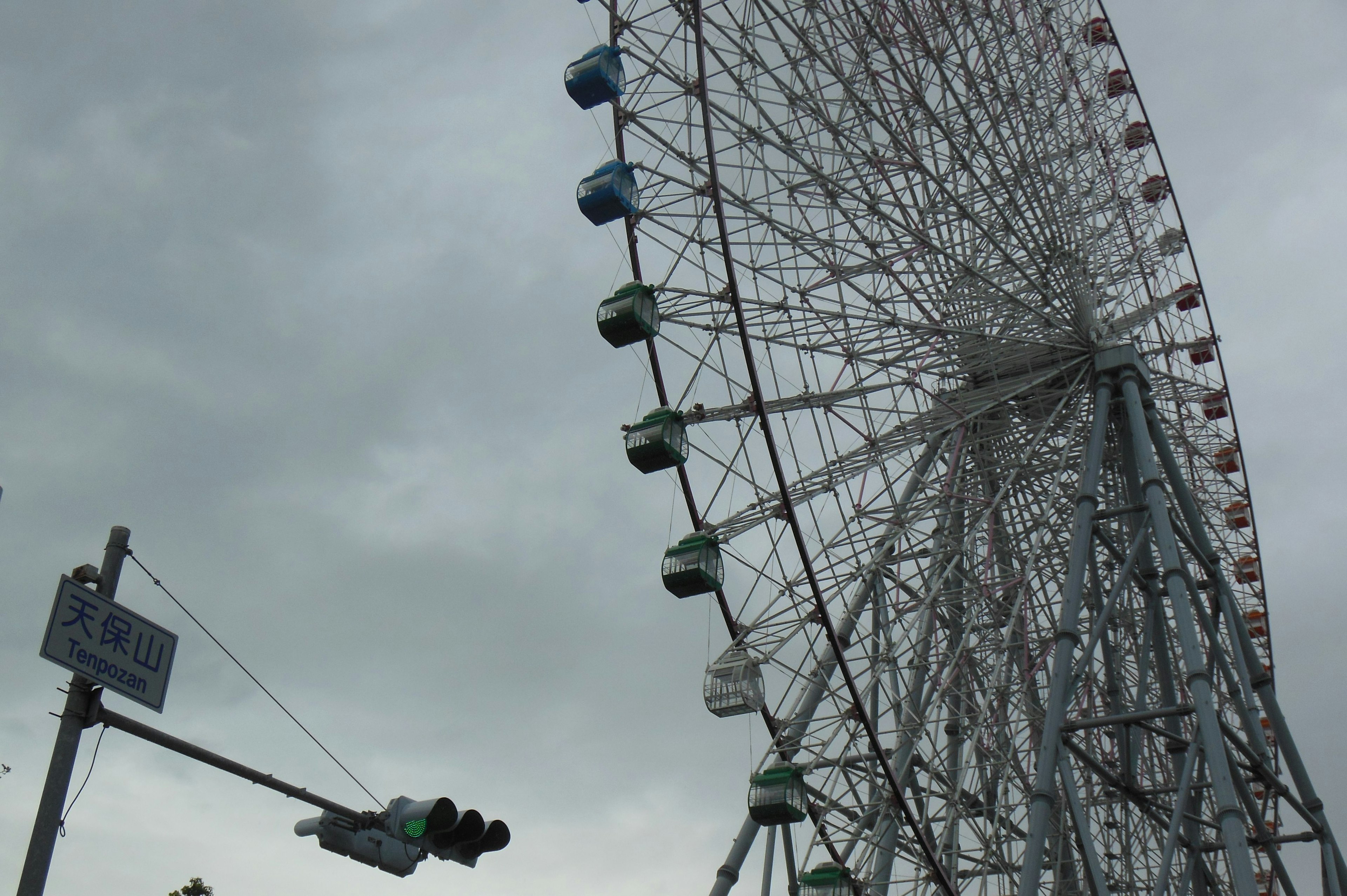 Tampilan samping dari roda ferris di bawah langit mendung dengan lampu lalu lintas di dekatnya