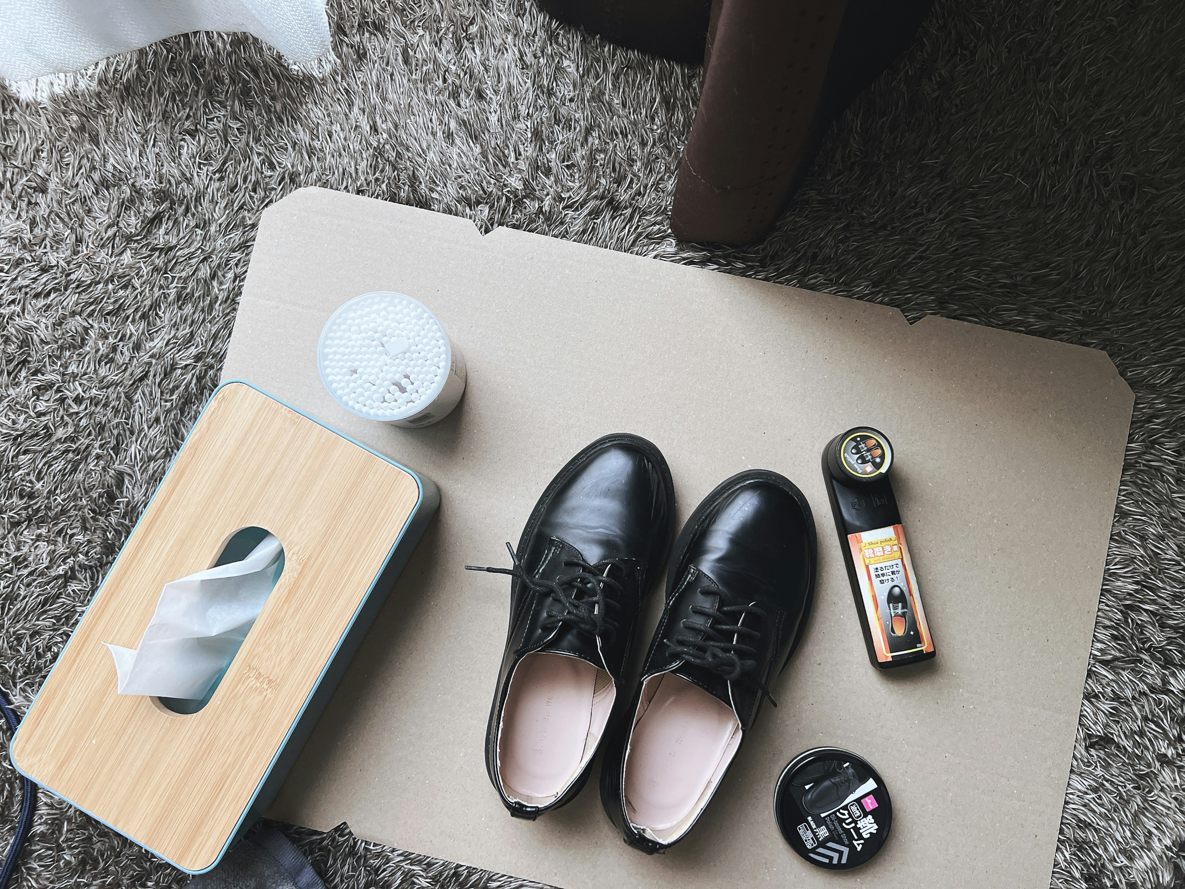 Chaussures noires à côté d'une boîte de mouchoirs et d'une boîte de crème sur un tapis