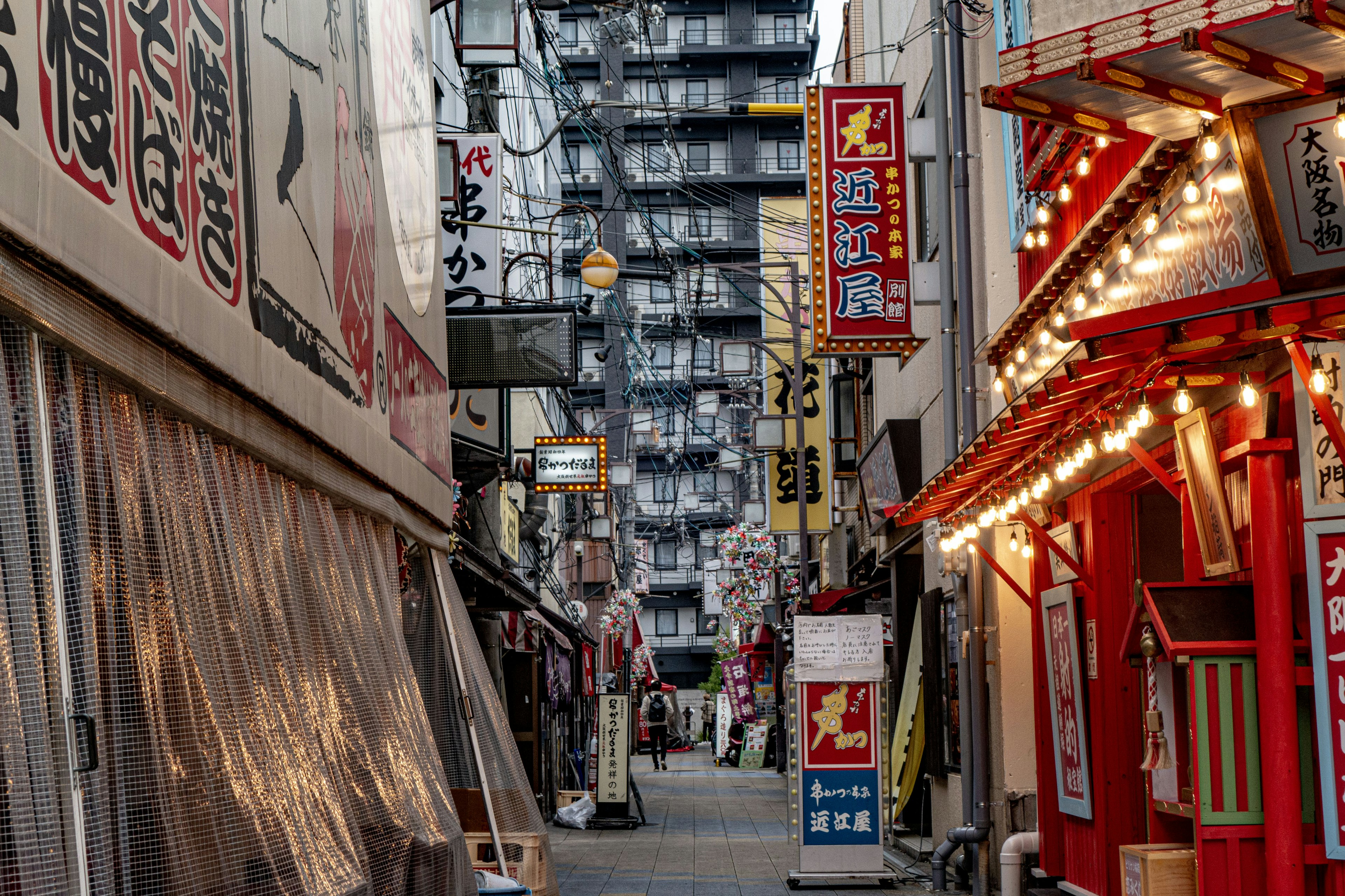 Narrow alley with restaurants and storefronts featuring bright signs