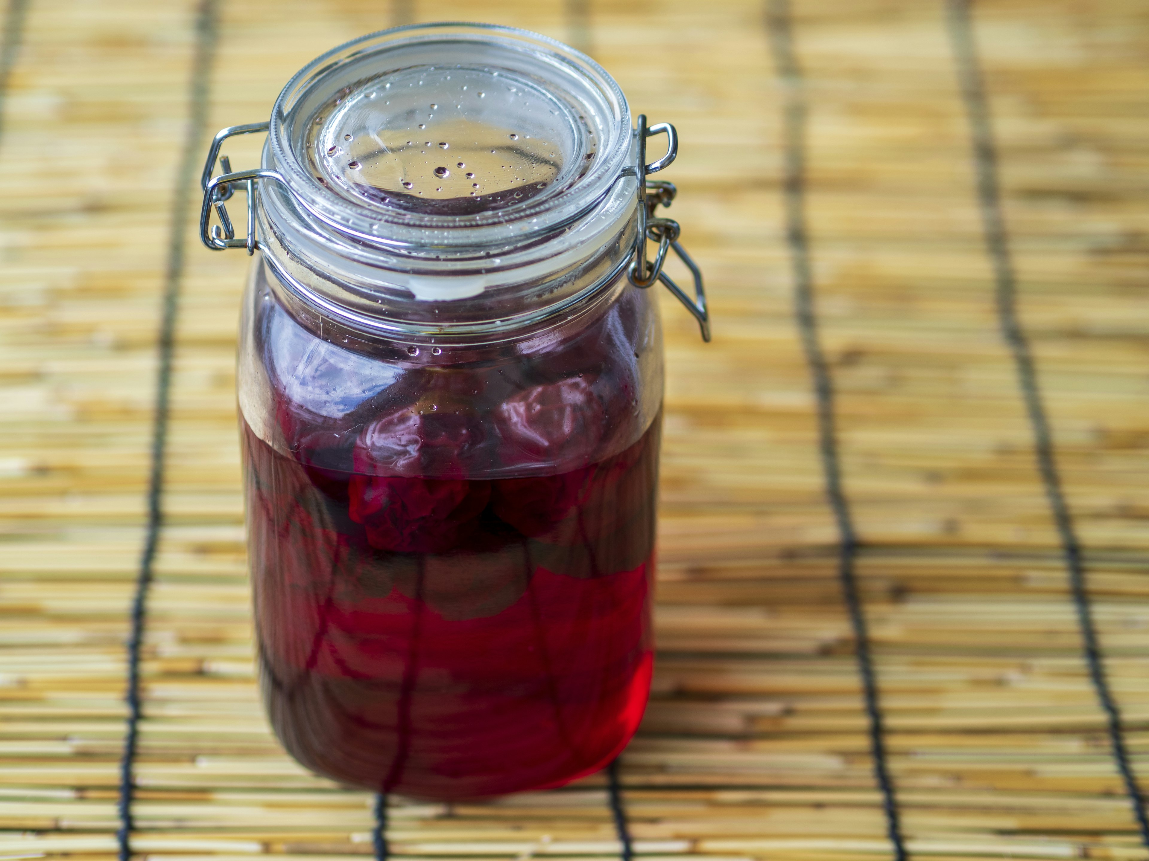 Sebuah toples kaca berisi cairan merah diletakkan di atas tikar bambu