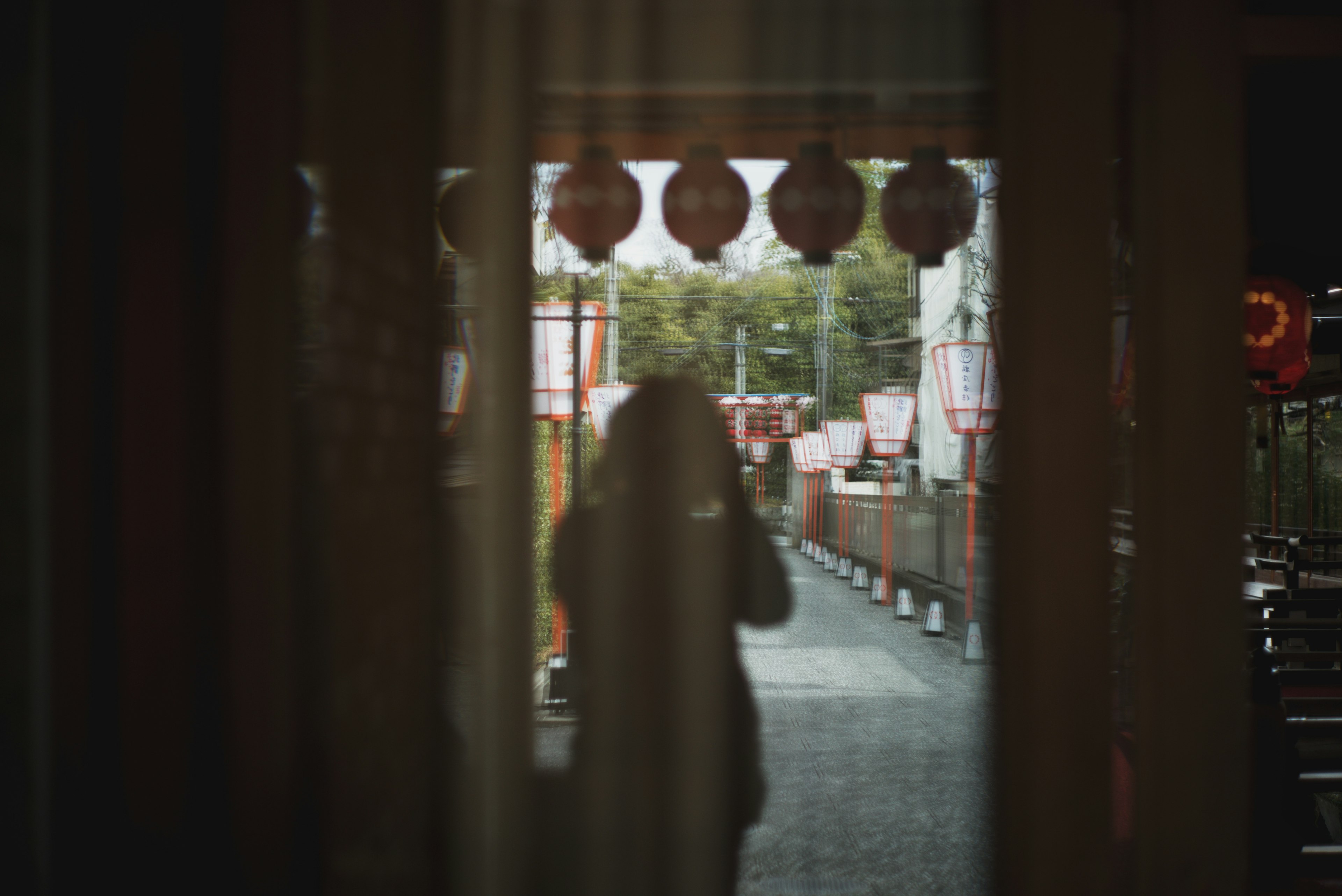 Silhouette di una persona dietro una tenda con lanterne rosse sullo sfondo