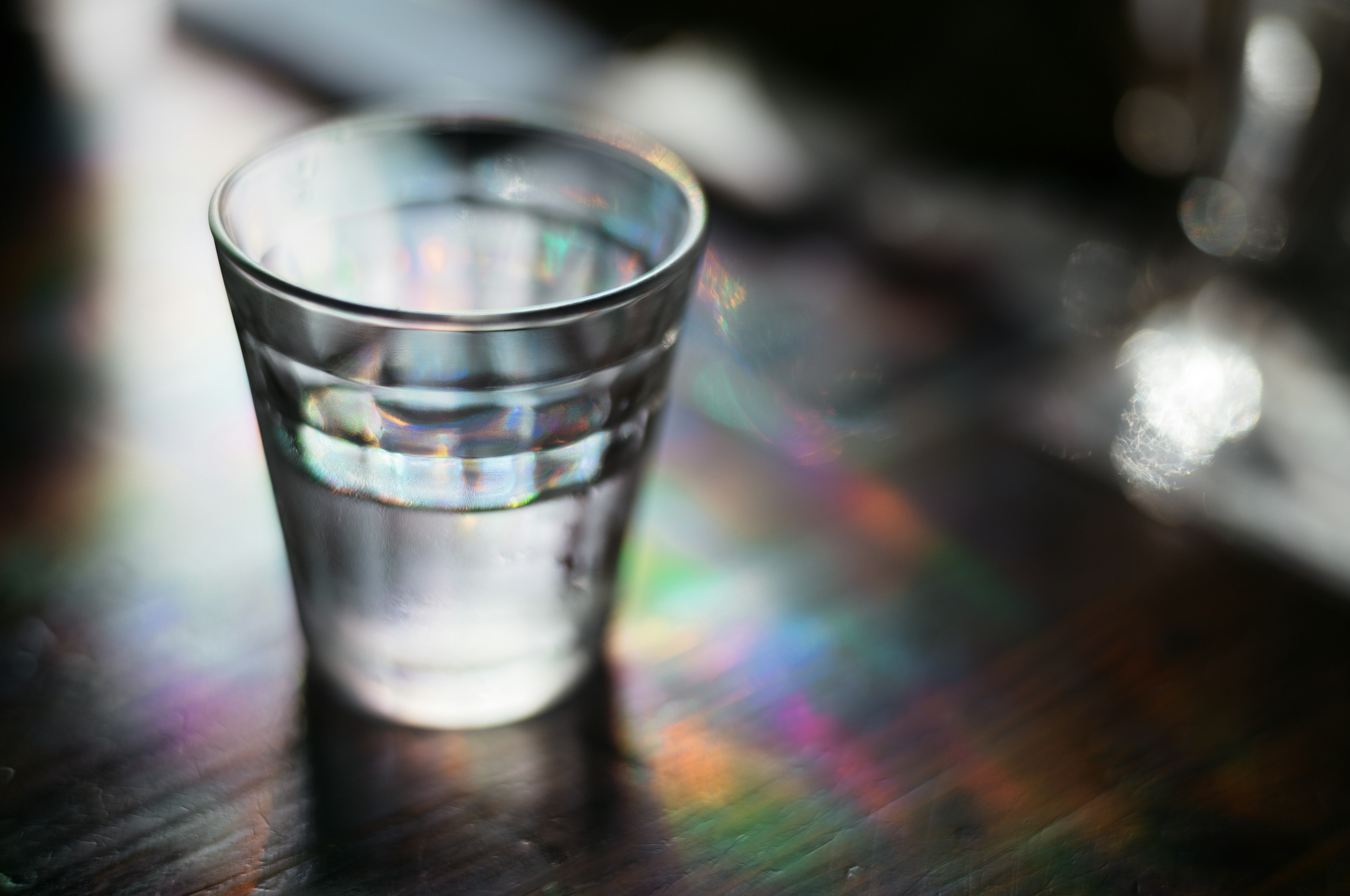 Transparentes Glas mit Wasser und Regenbogenreflexionen auf dem Tisch