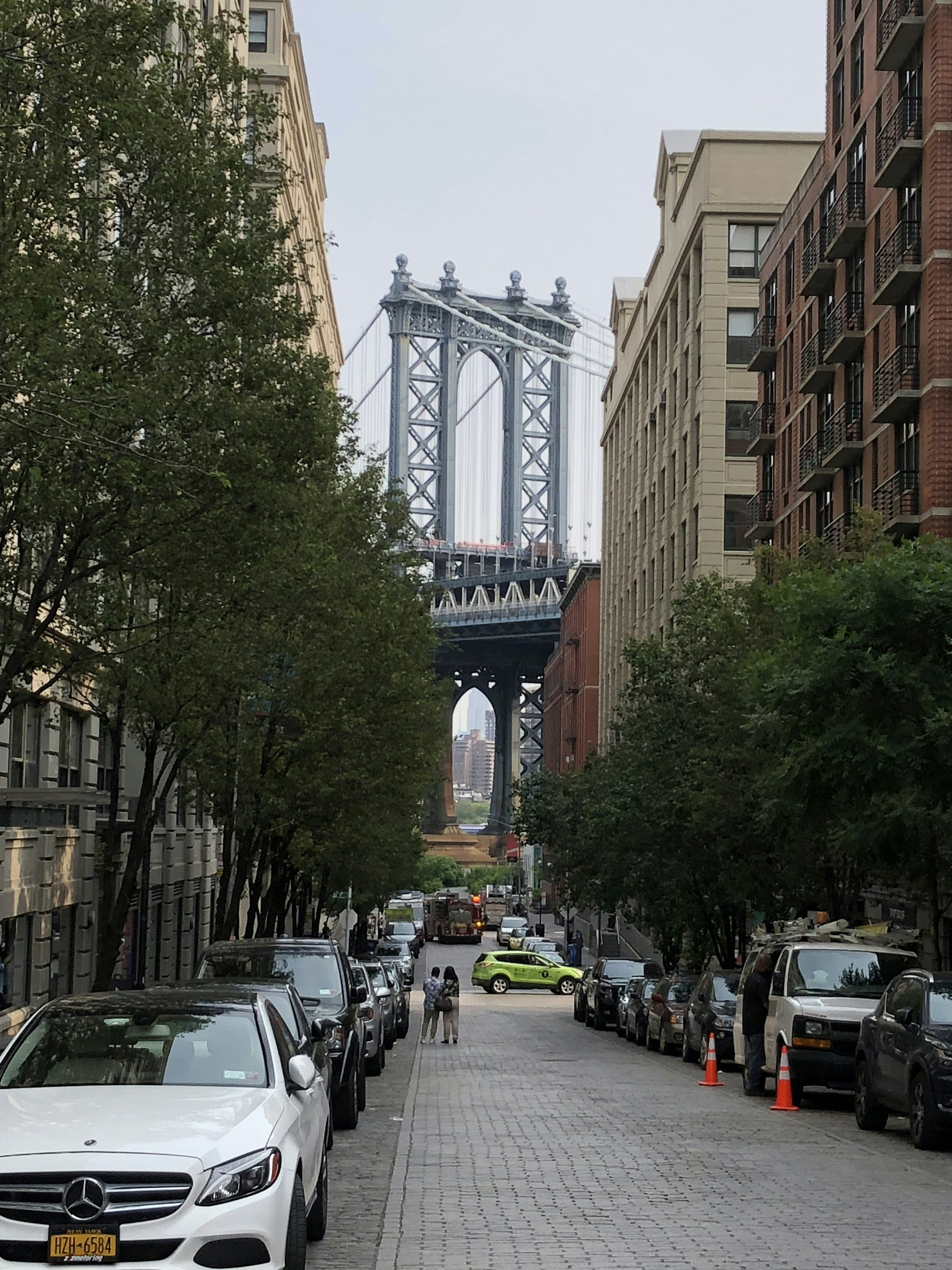 Vista del ponte di Manhattan da una strada fiancheggiata da auto e alberi