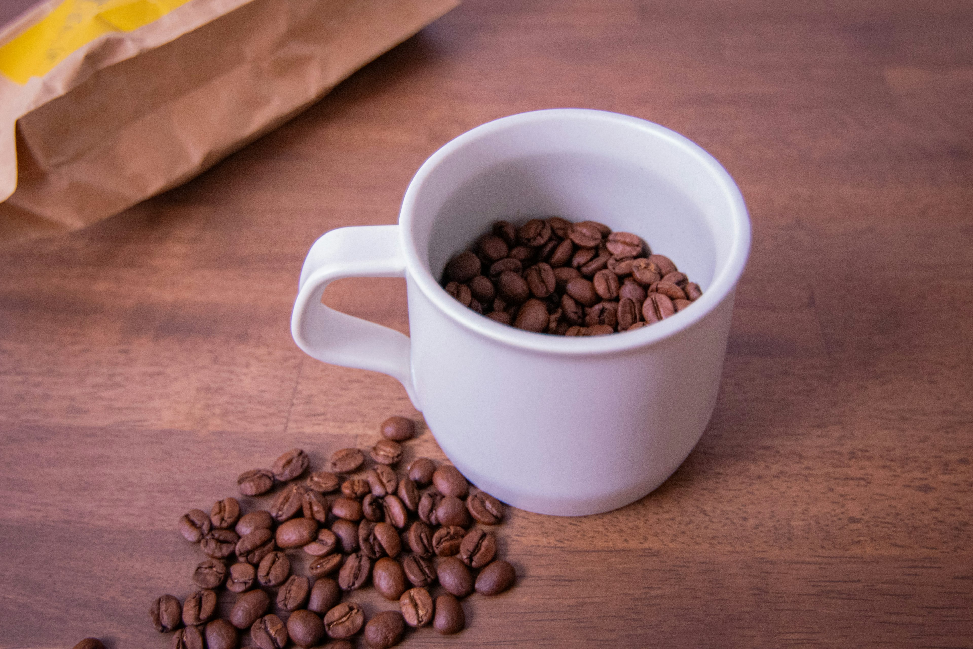 Tasse blanche remplie de grains de café et grains de café éparpillés autour