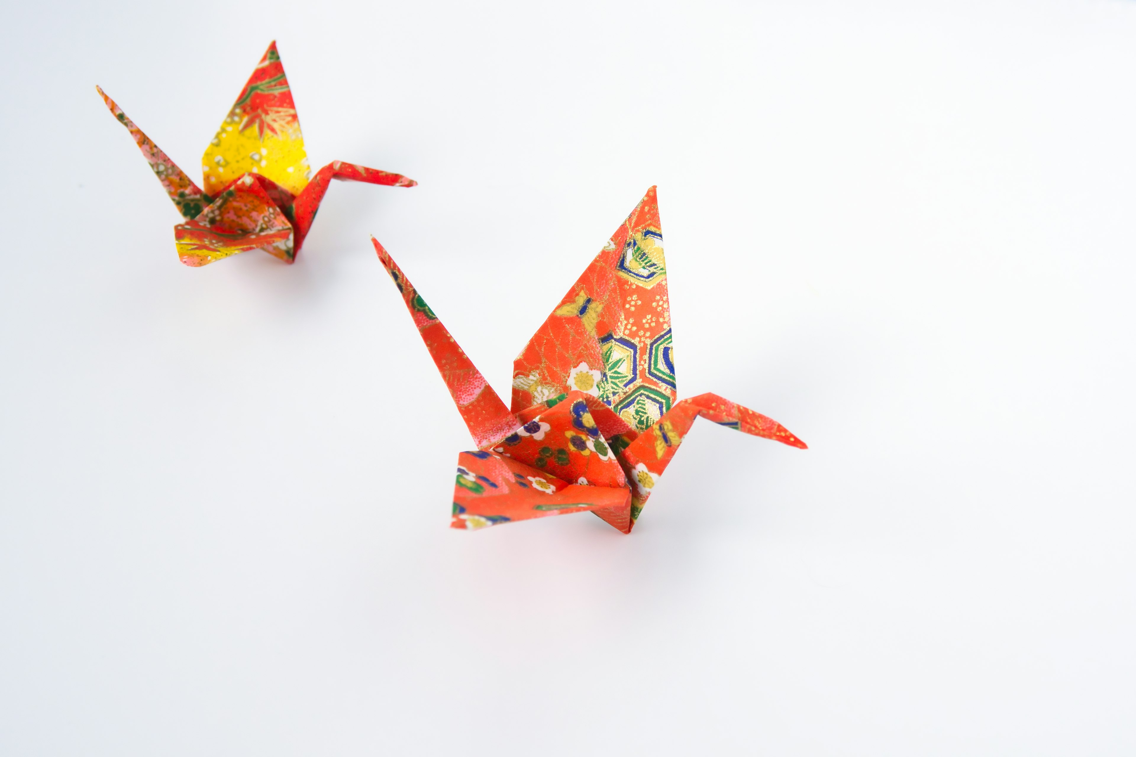 Deux grues en origami de couleurs rouge et orange placées sur un fond blanc