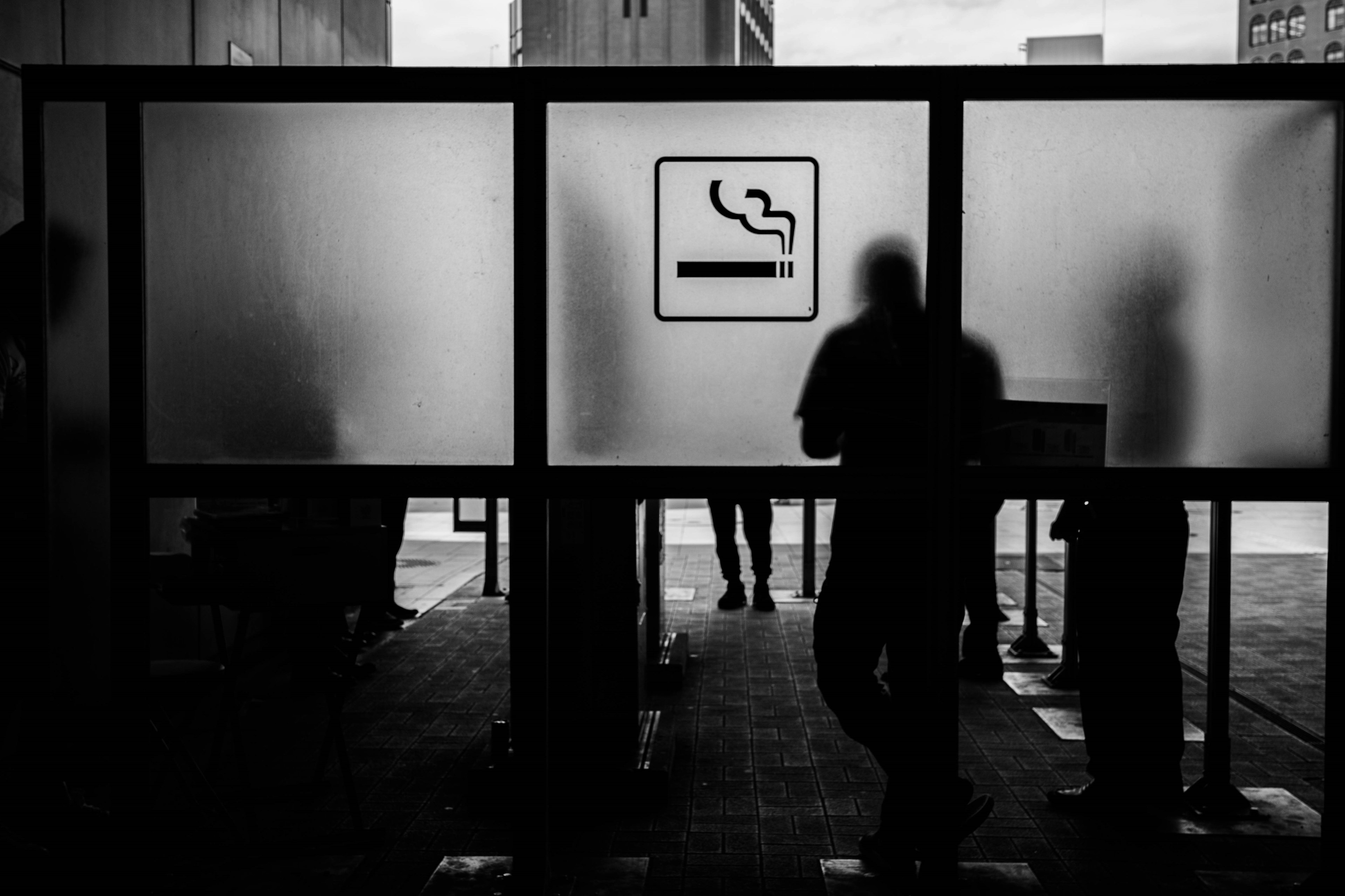 Silhouettes of people standing in front of frosted panels with a no smoking sign