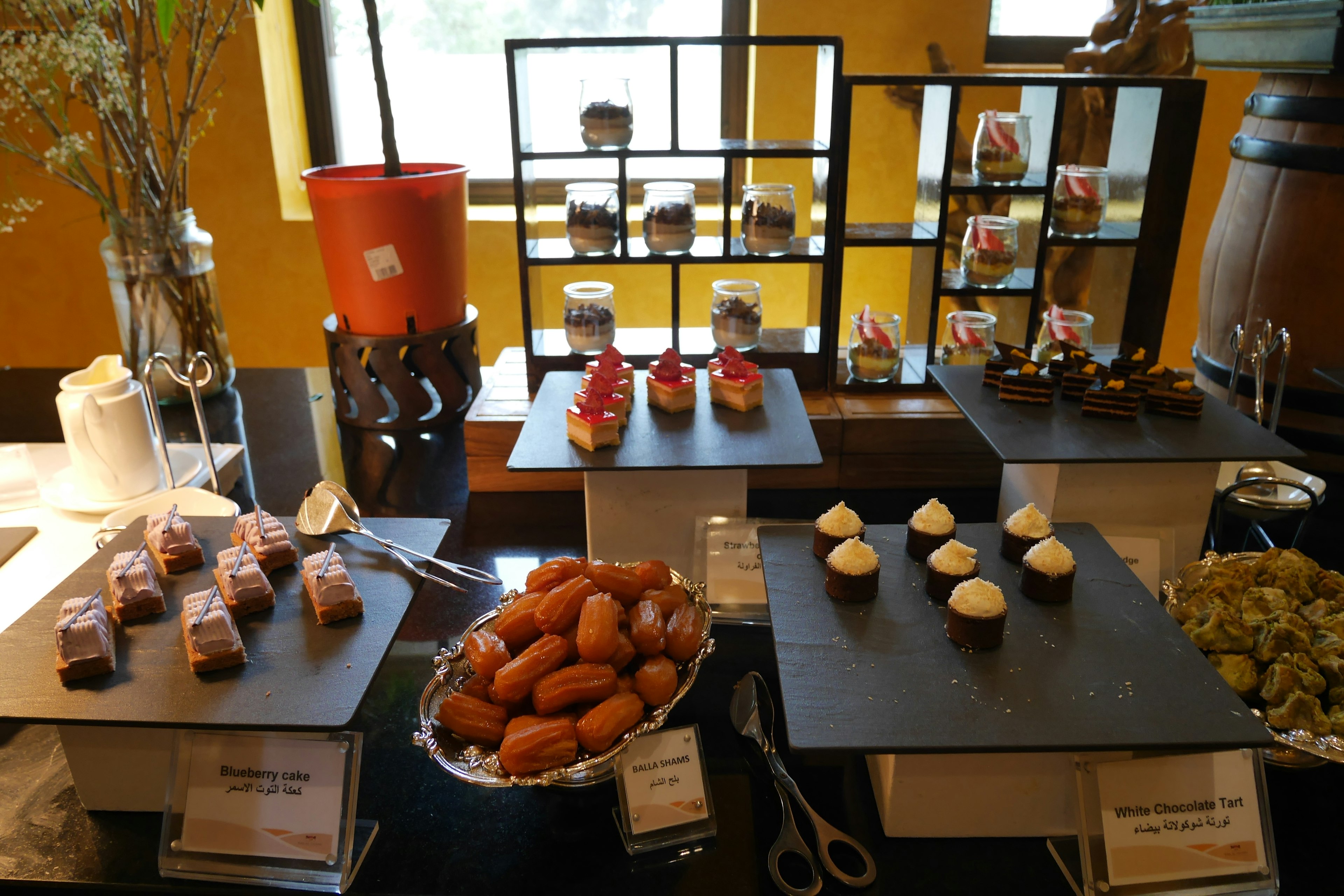 A buffet table displaying various desserts including cupcakes and pastries with a red candle and black display stands