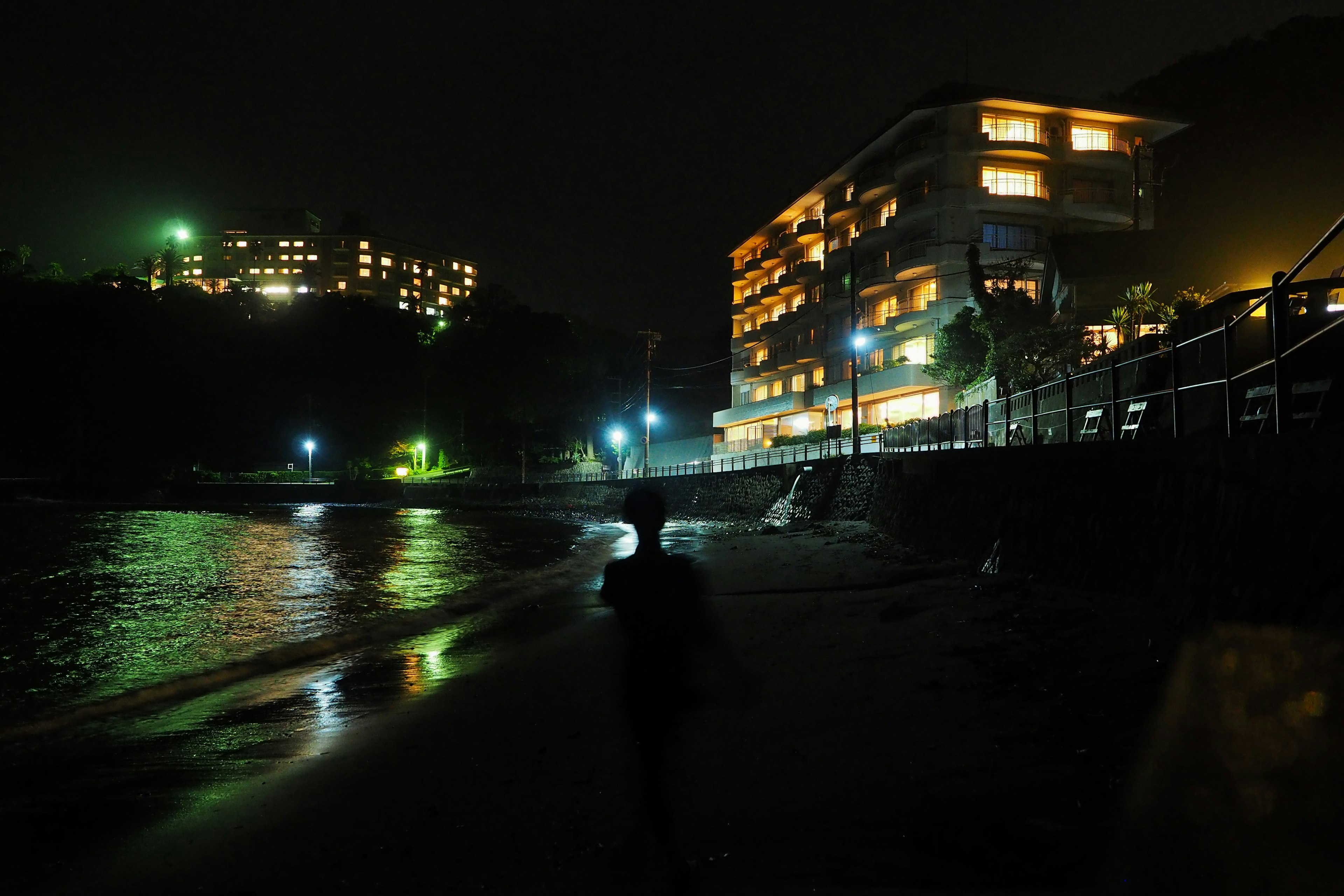 夜の海岸に立つ人と明かりの灯る建物