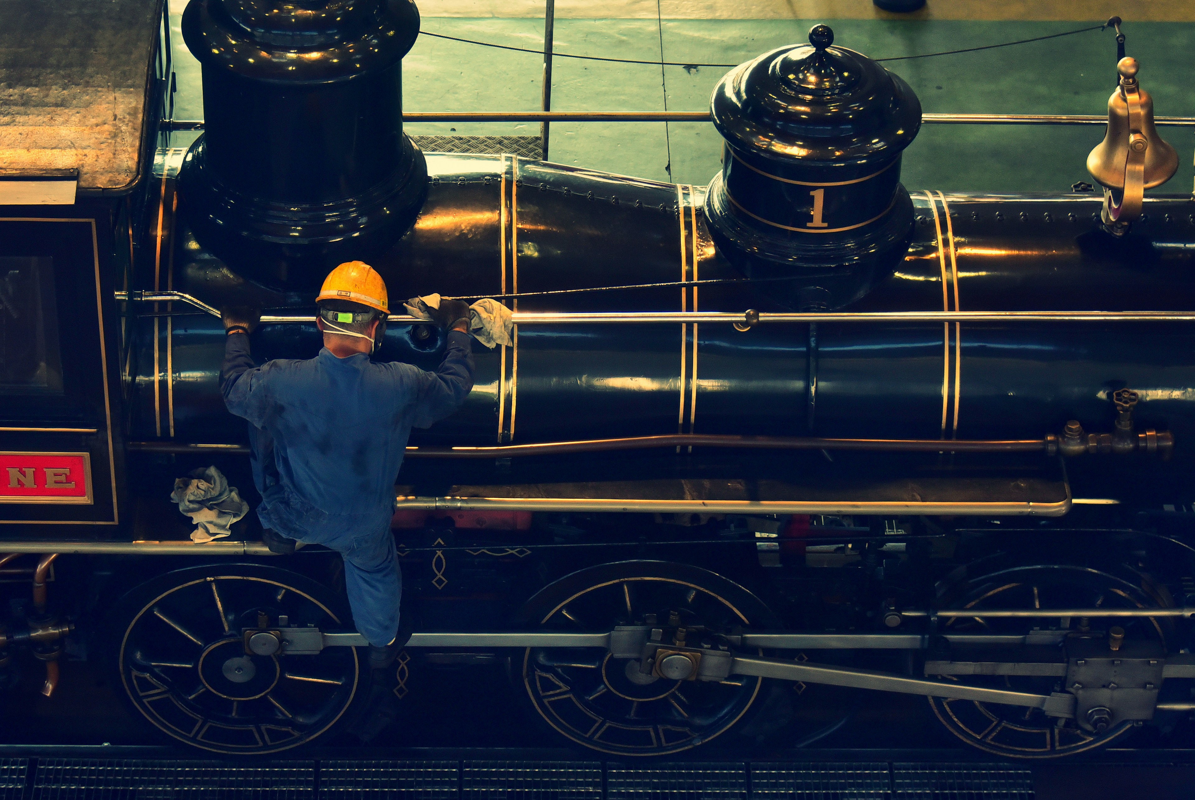 Worker performing maintenance on a steam locomotive wearing a yellow helmet inspecting the side of the engine