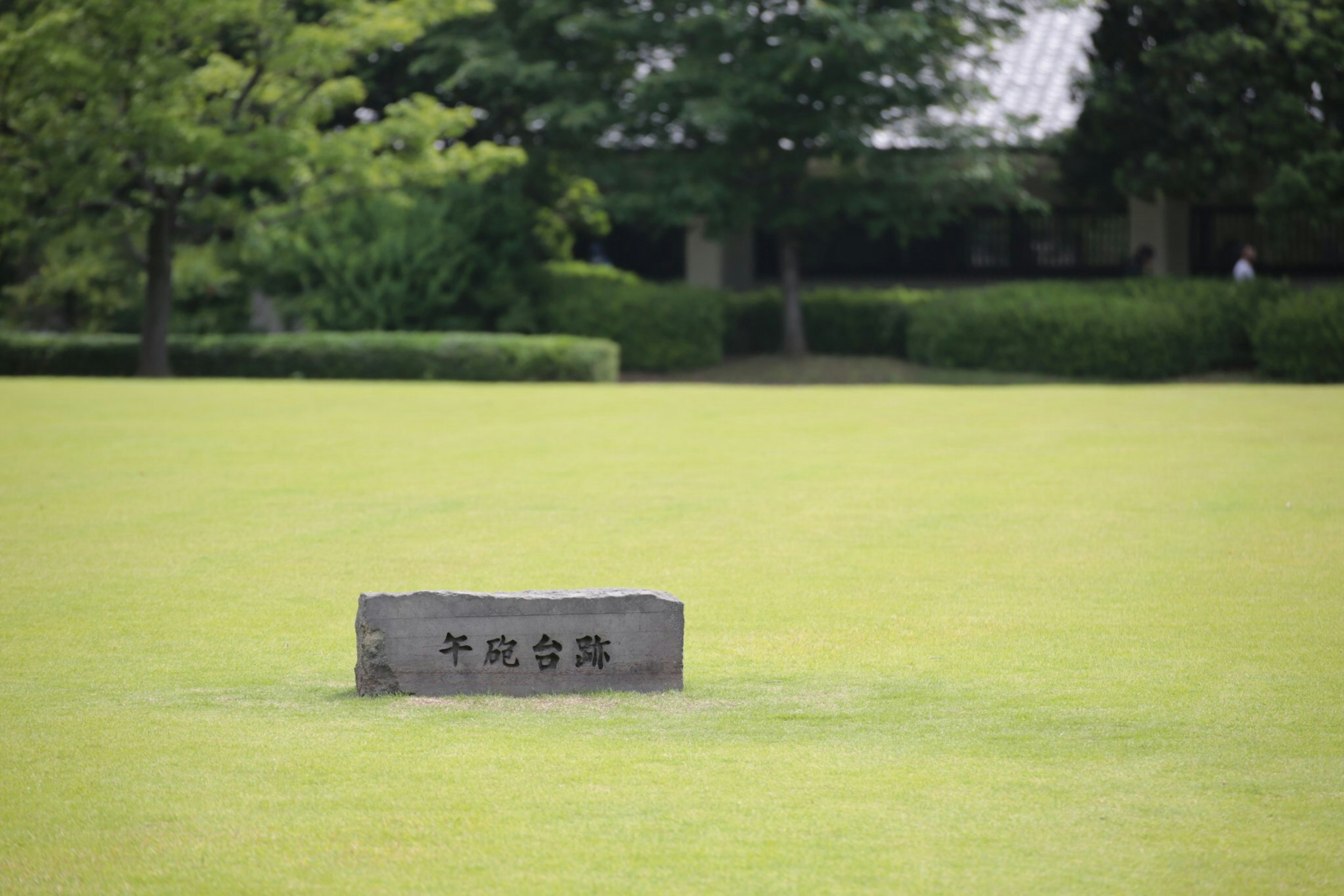 緑の芝生の上にある石碑と周囲の木々