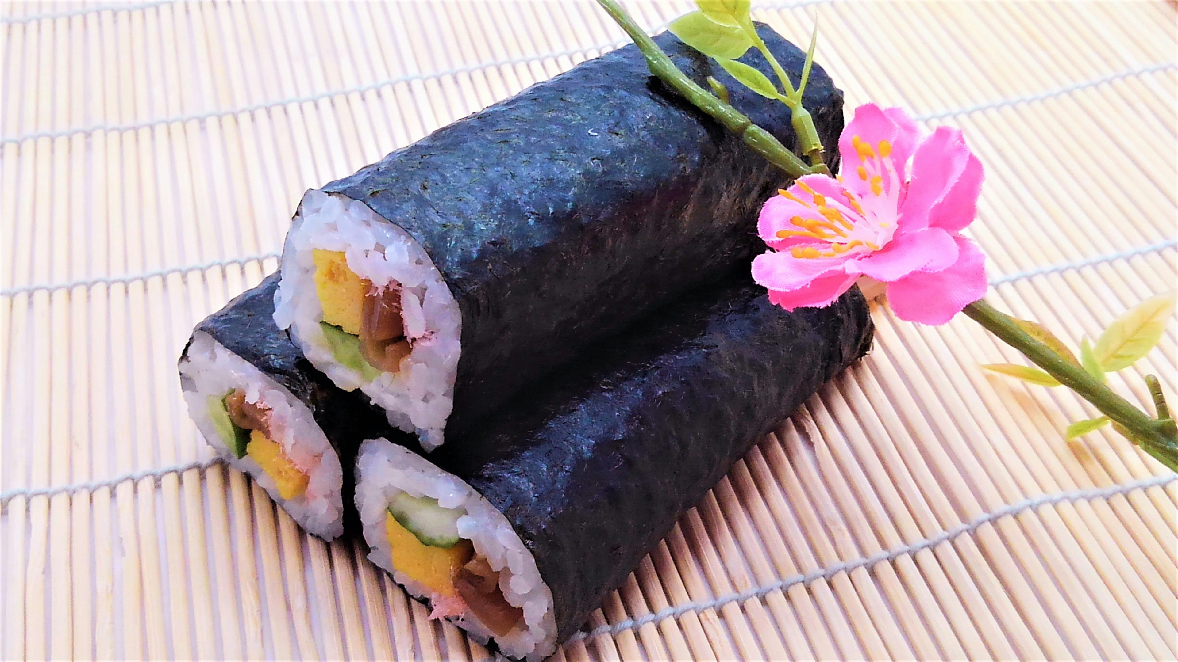 Three sushi rolls filled with colorful ingredients and a pink flower