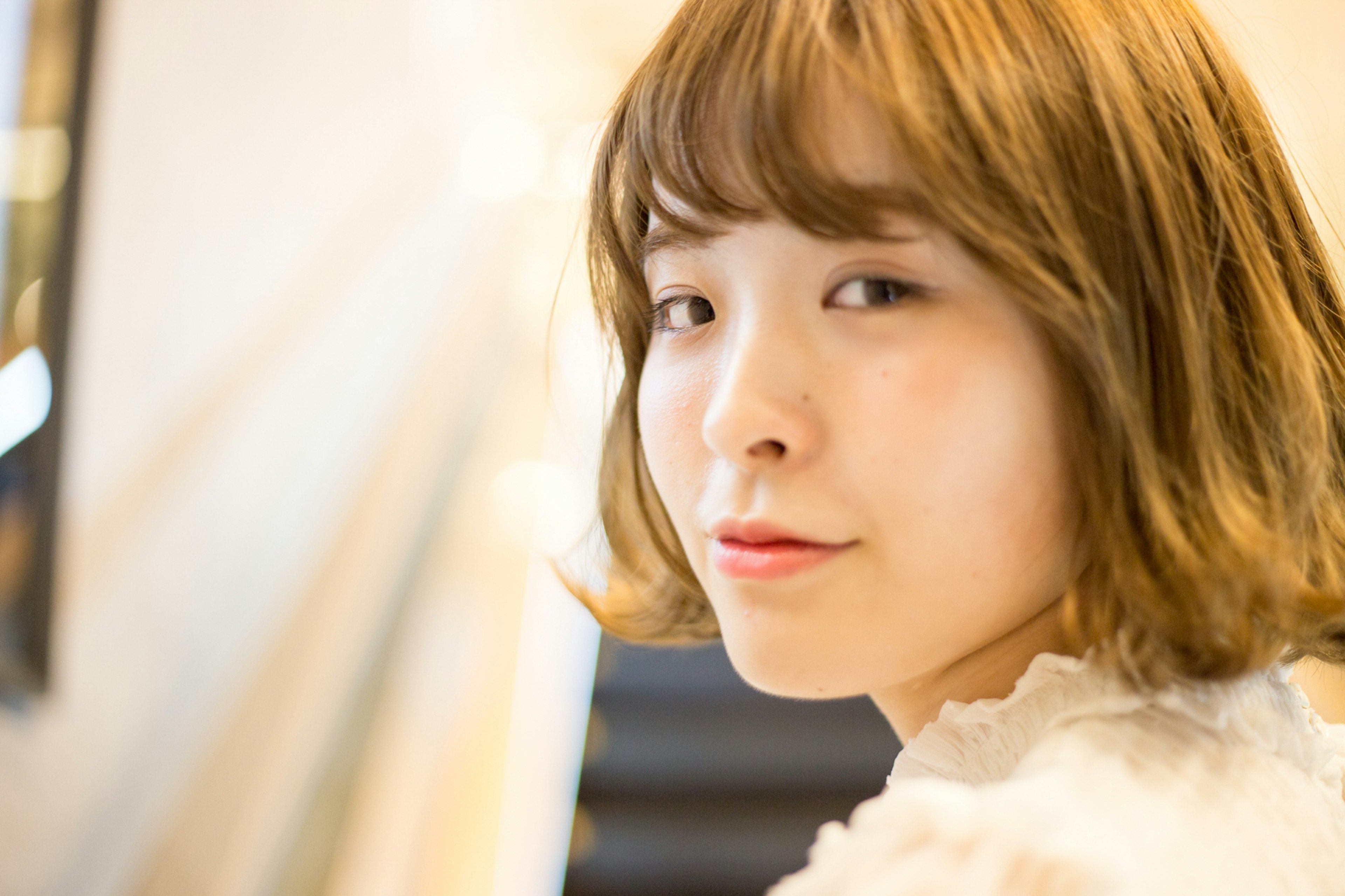 A young woman smiling at the camera She has short brown hair and is wearing a white top A staircase is softly visible in the background