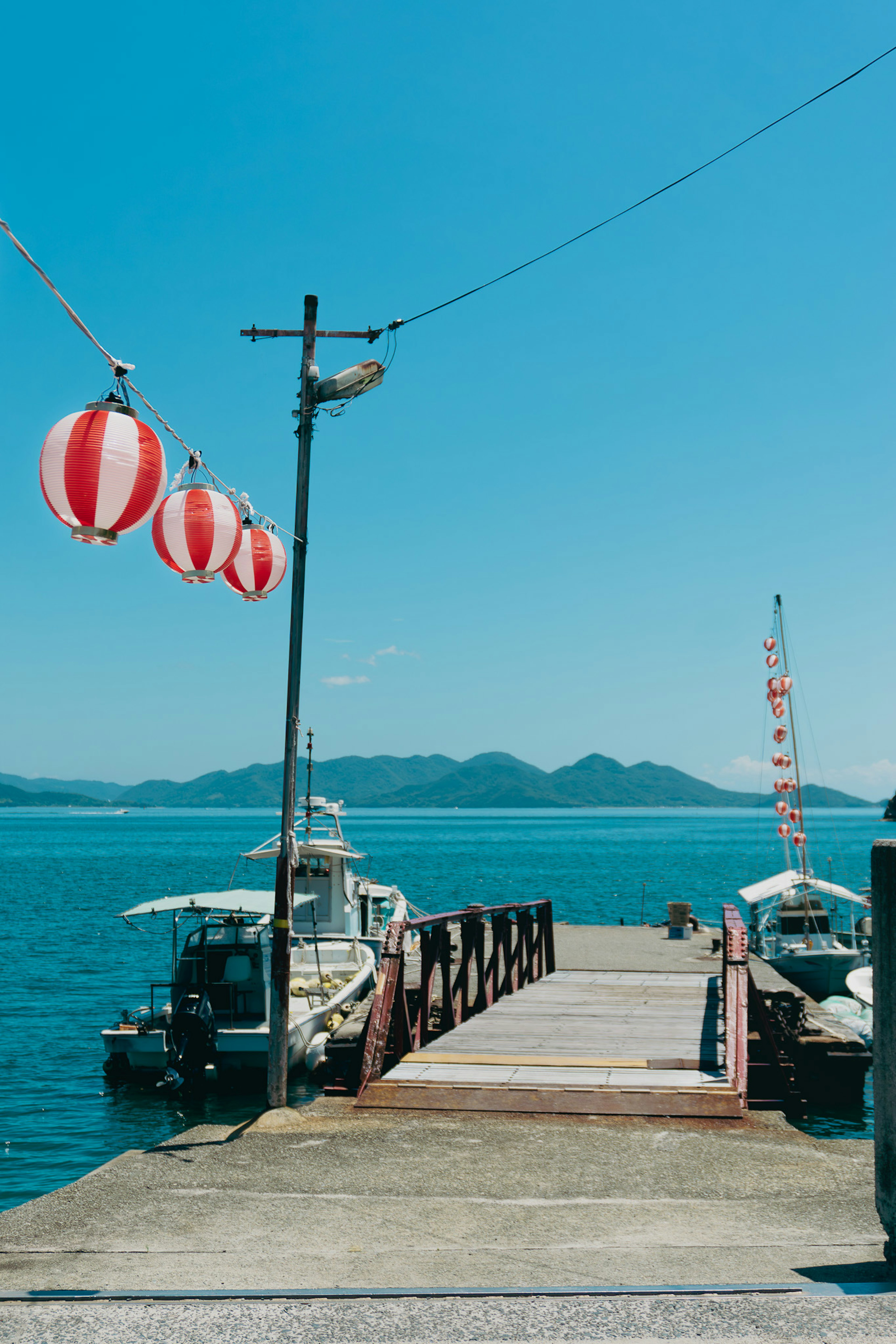 Pier with red and white lanterns overlooking blue water and mountains