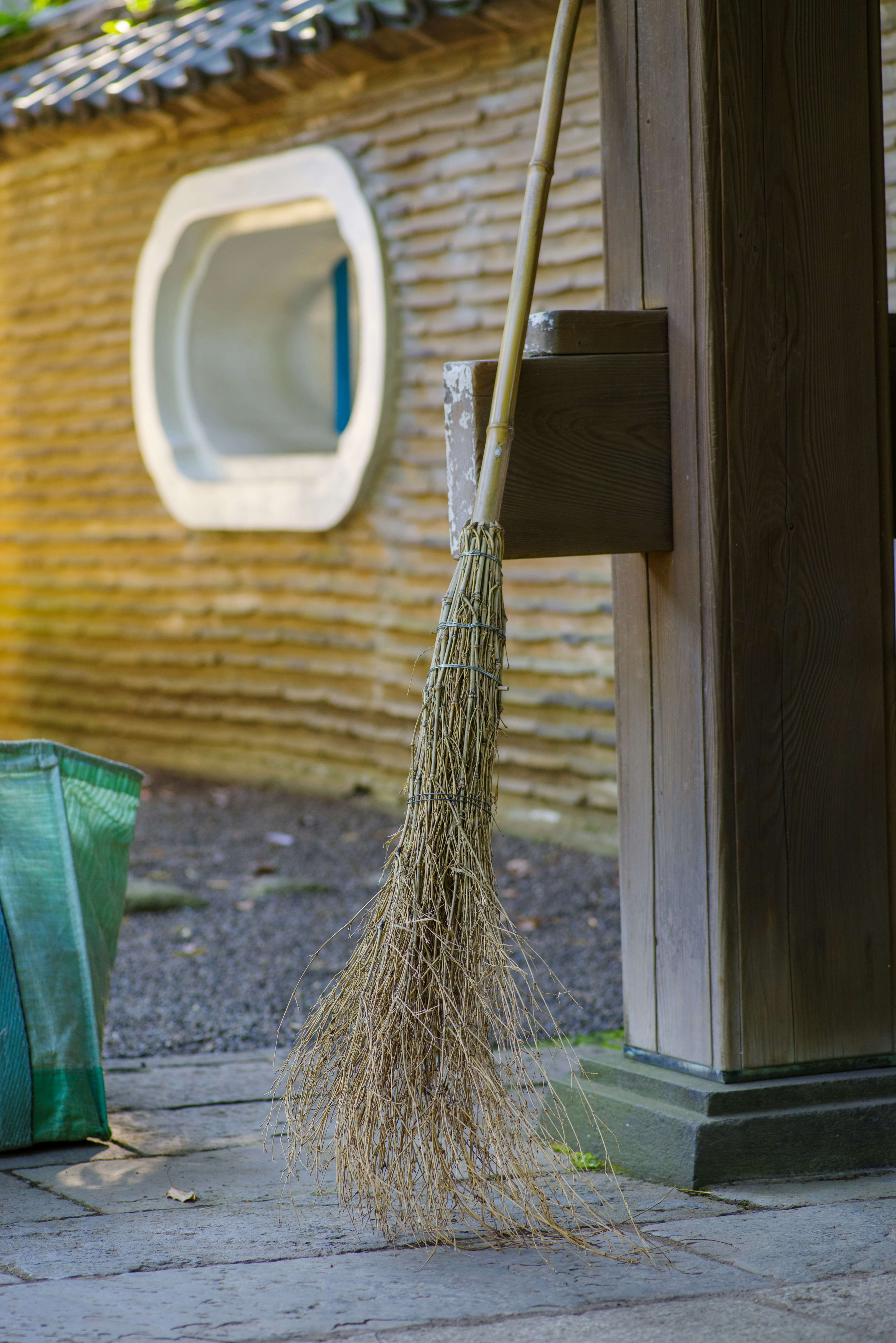 Broom hanging beside a wooden post with a traditional Japanese building in the background