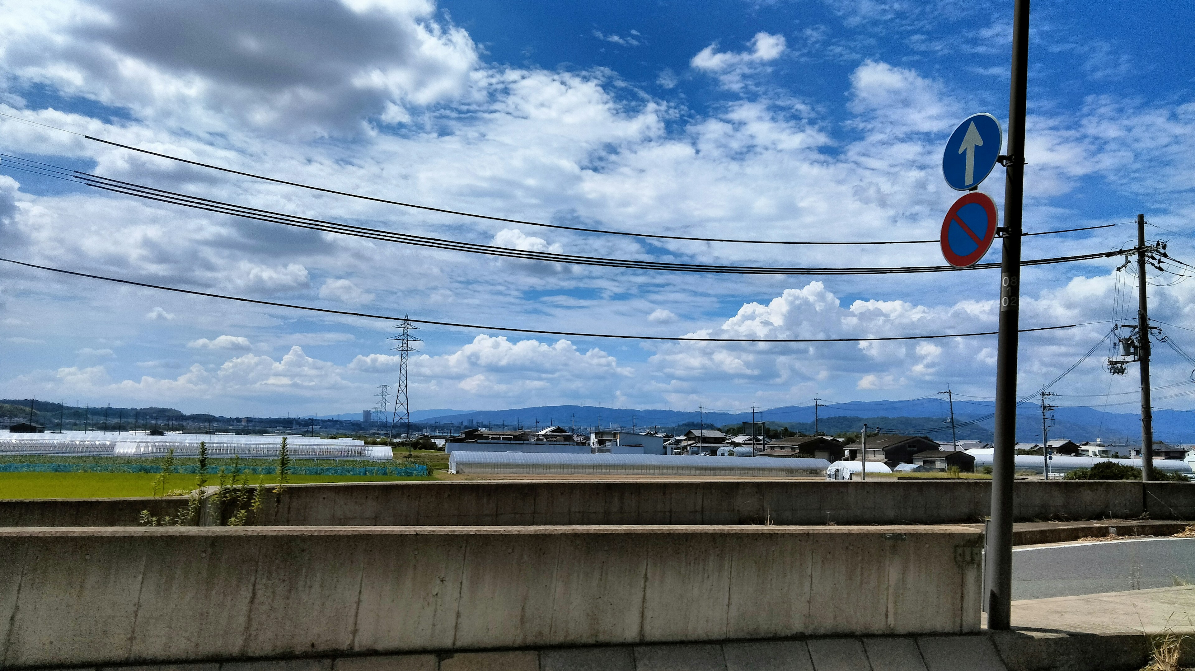 Vista panoramica di campi sotto un cielo azzurro con nuvole bianche e segnali stradali