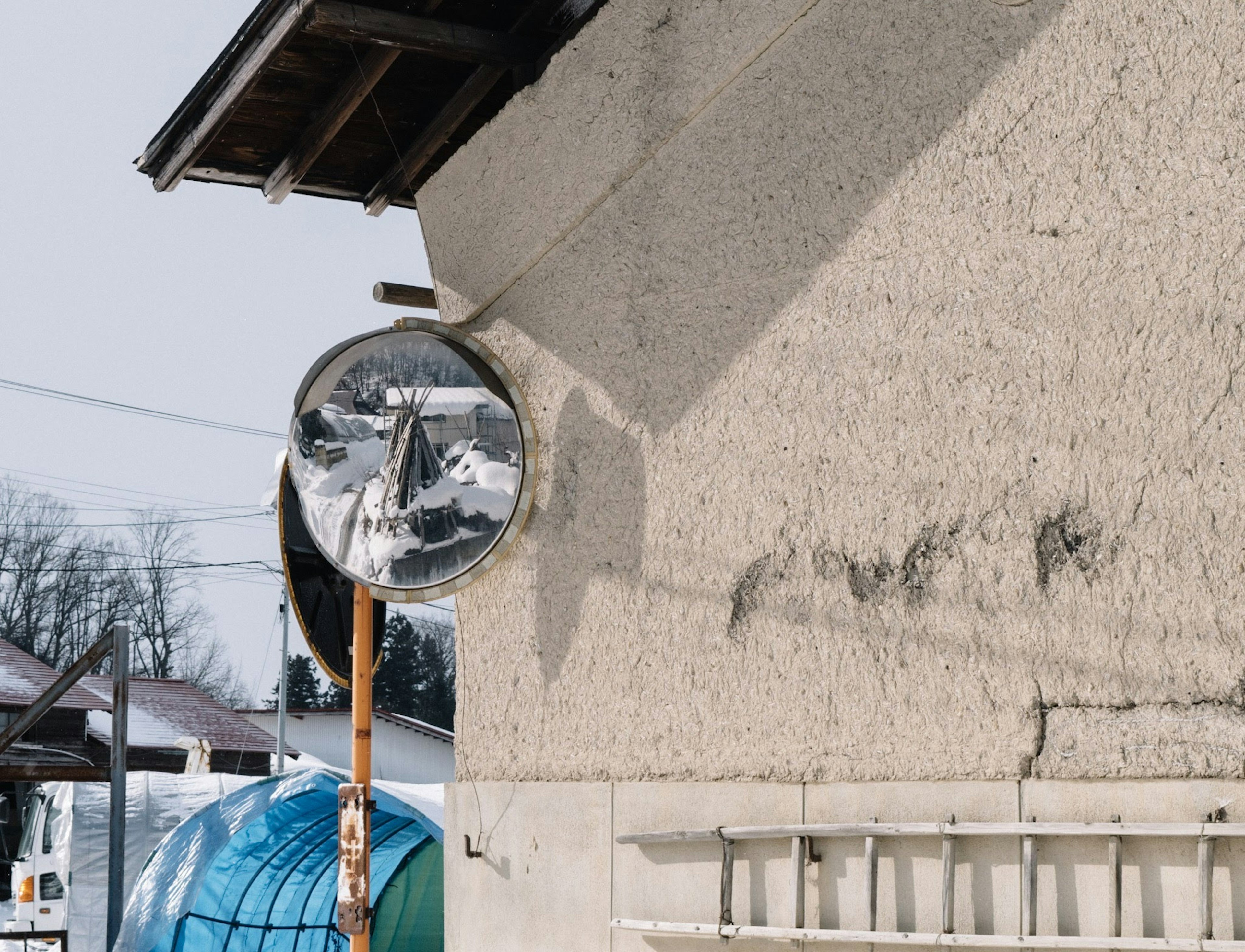 Round mirror mounted on a white wall casting a shadow nearby blue tent