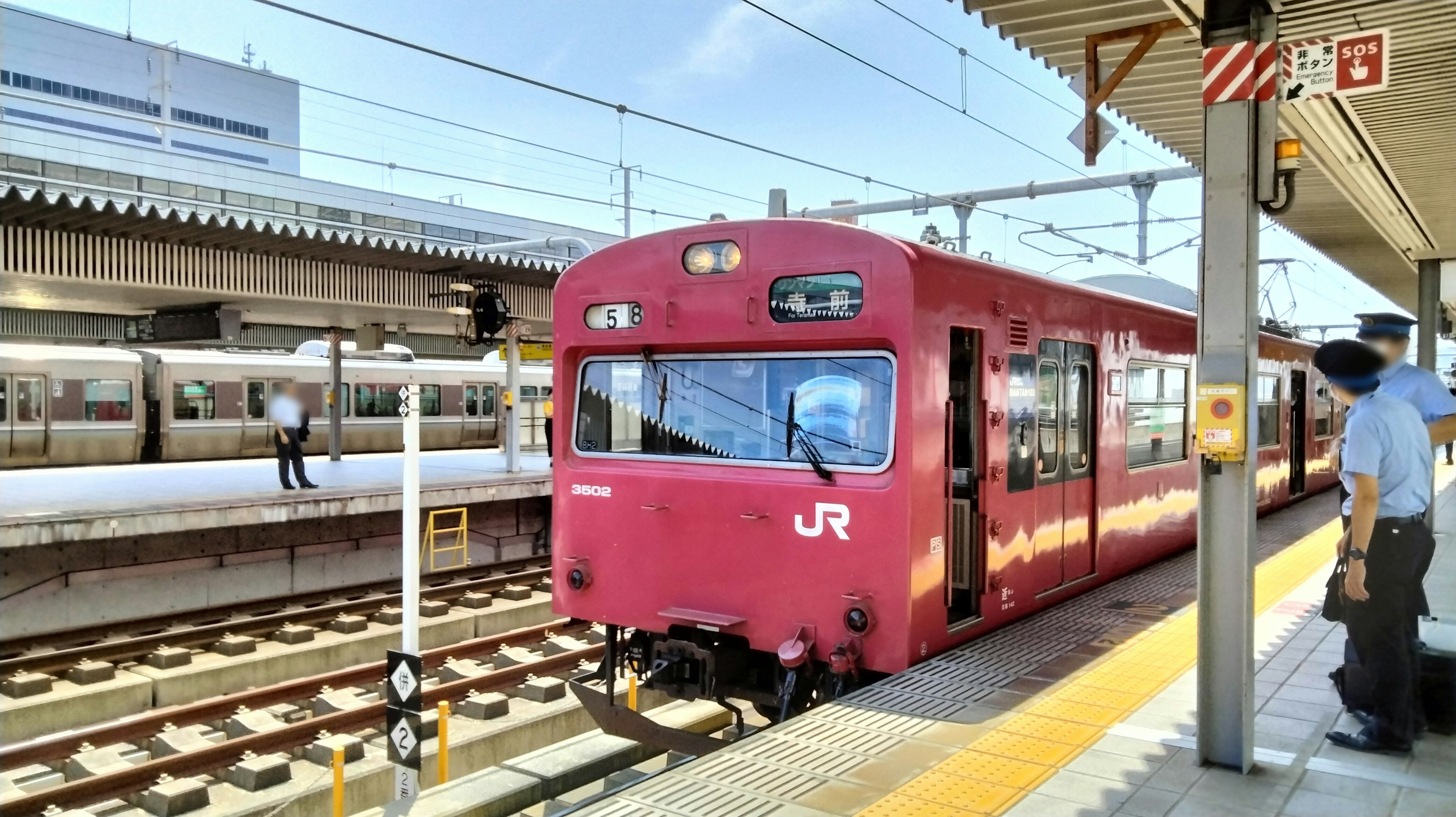 Sebuah kereta JR merah di stasiun dengan penumpang dan rel