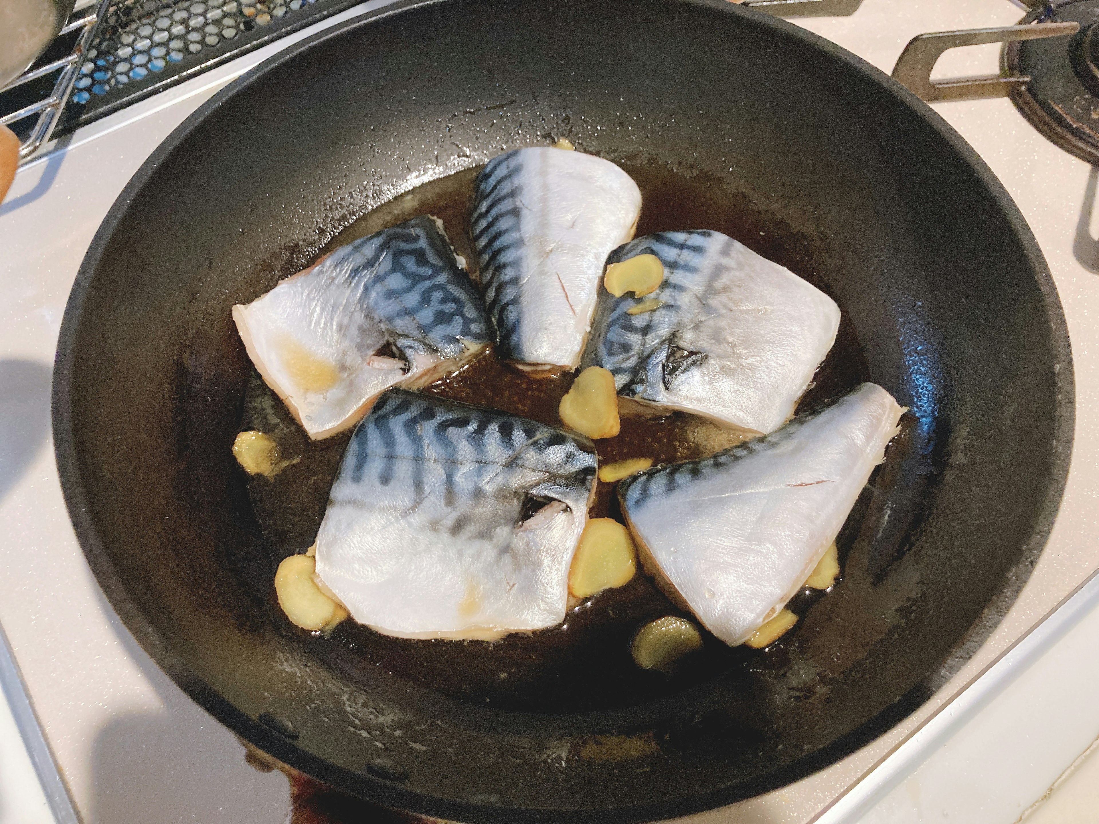 Fish fillets cooking in a frying pan with ginger slices