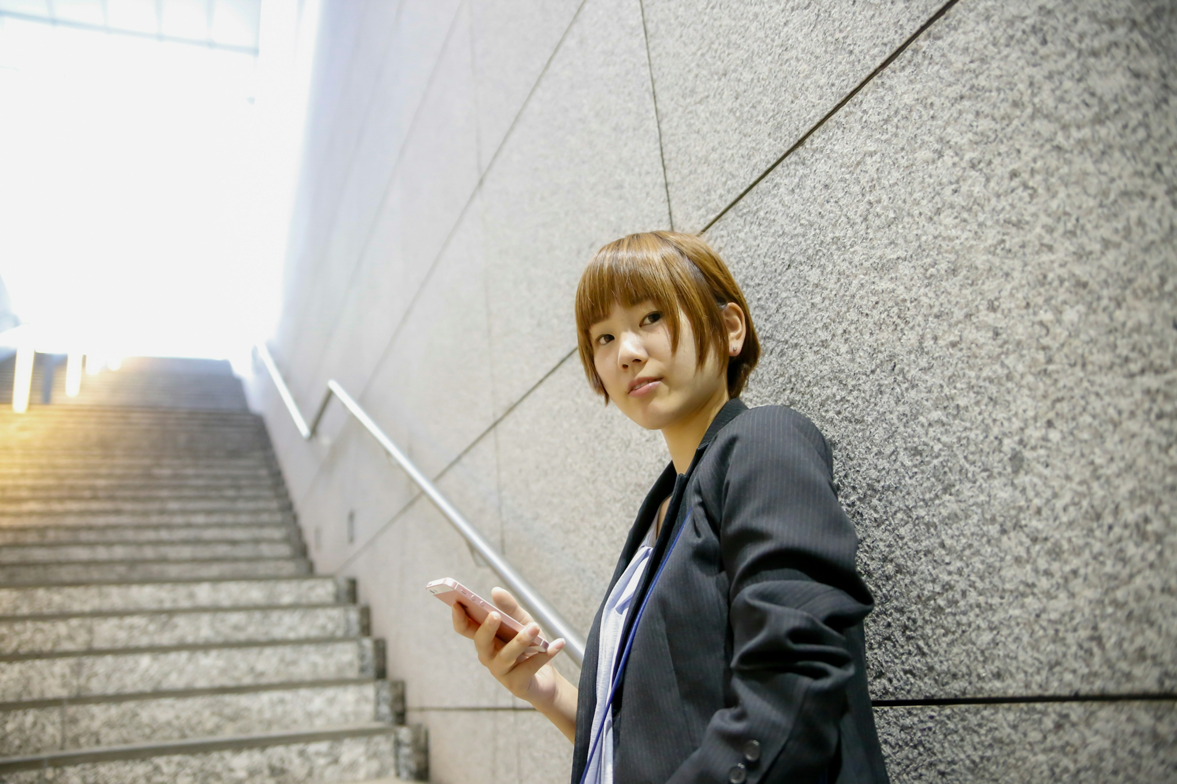 A woman leaning against a staircase holding a smartphone