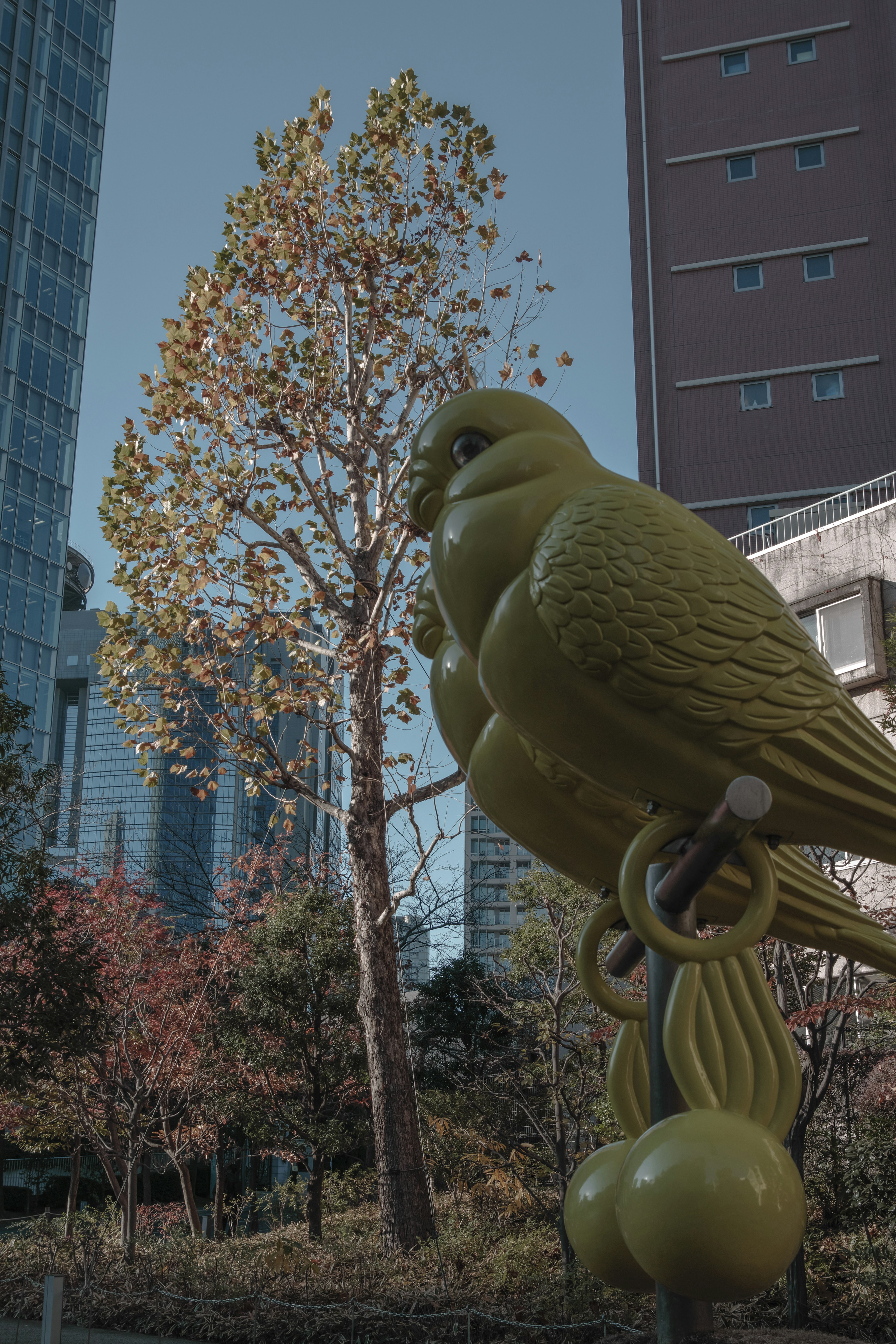 黄色い鳥の彫刻と背後の木々と高層ビルが見える都市の公園