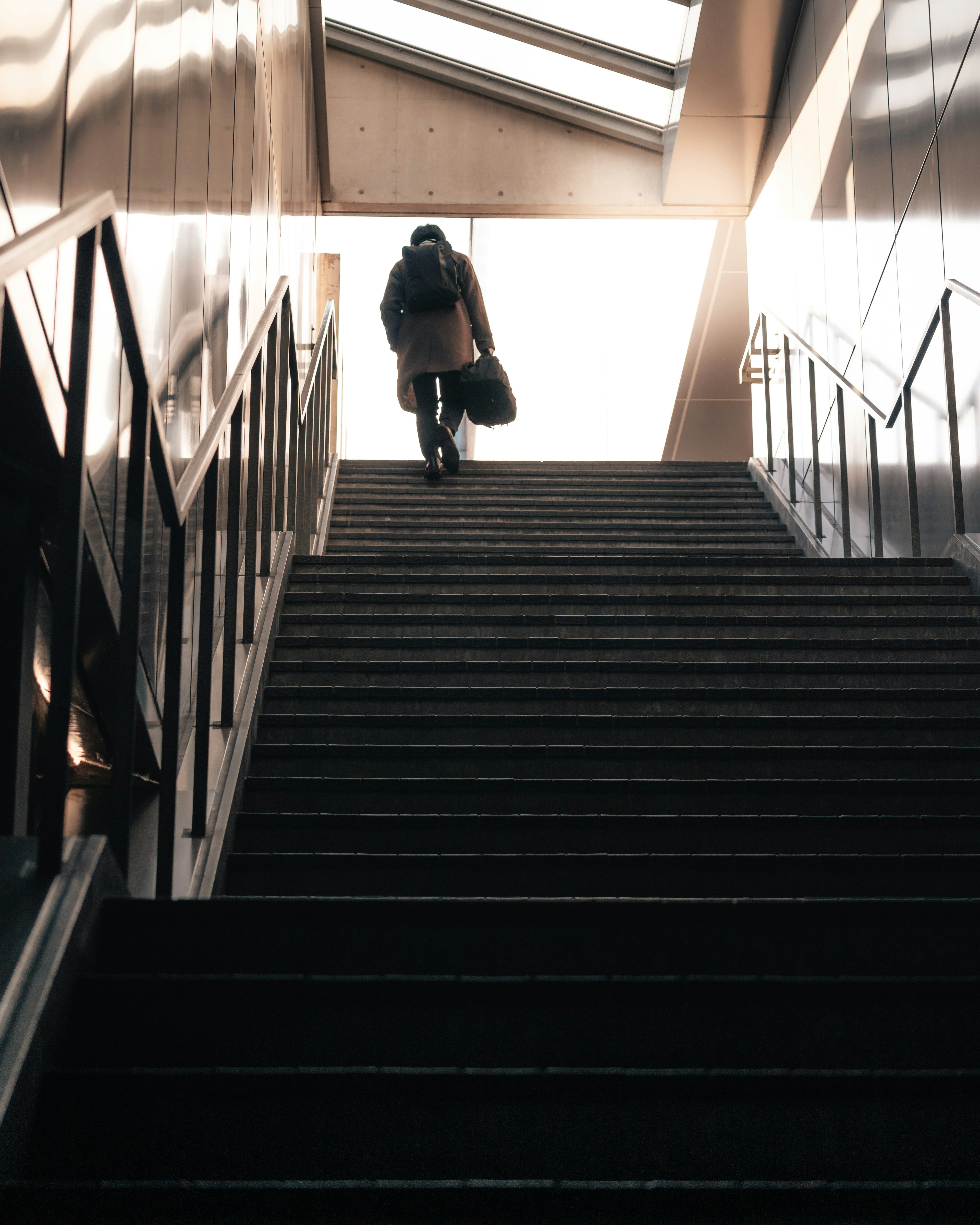 Silhouette of a person ascending stairs with bright light coming in