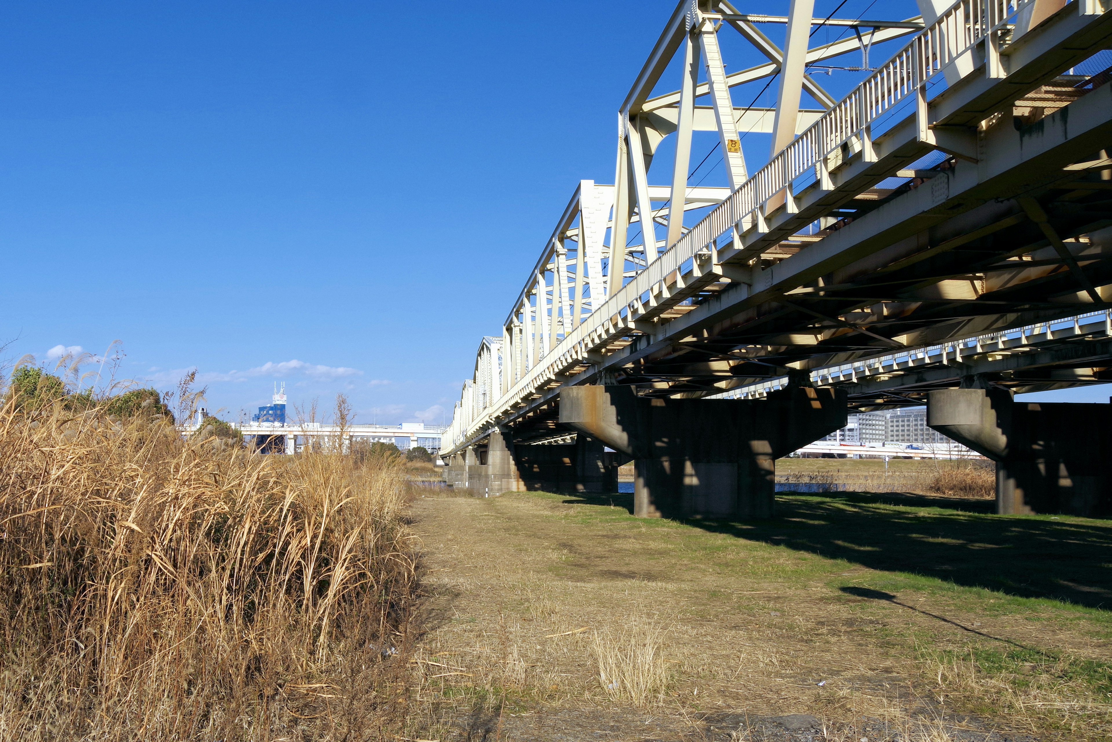 A view of a railway bridge under a blue sky featuring grass and dirt ground