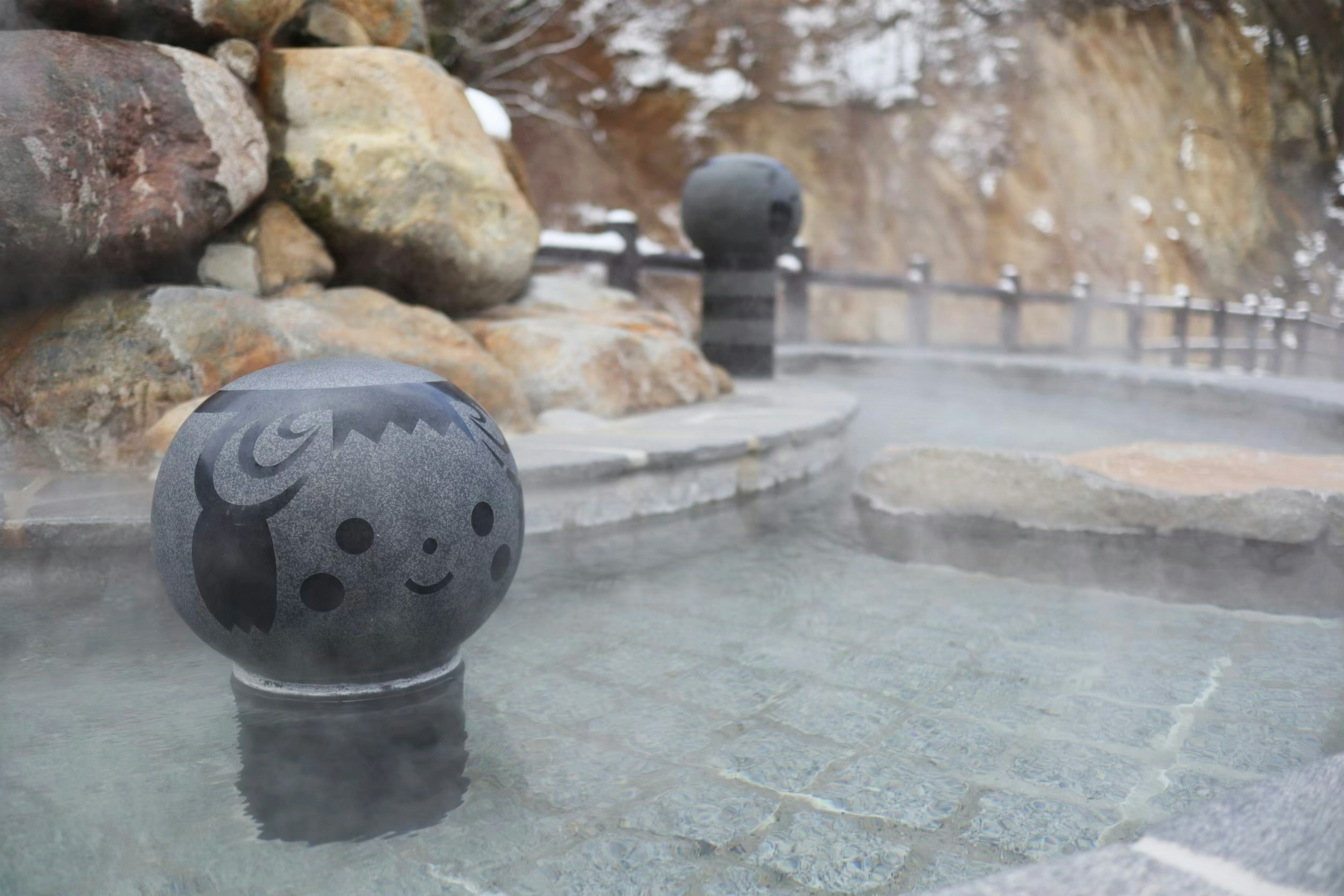 Sculptures sphériques noires avec des visages souriants dans une source chaude entourée de rochers