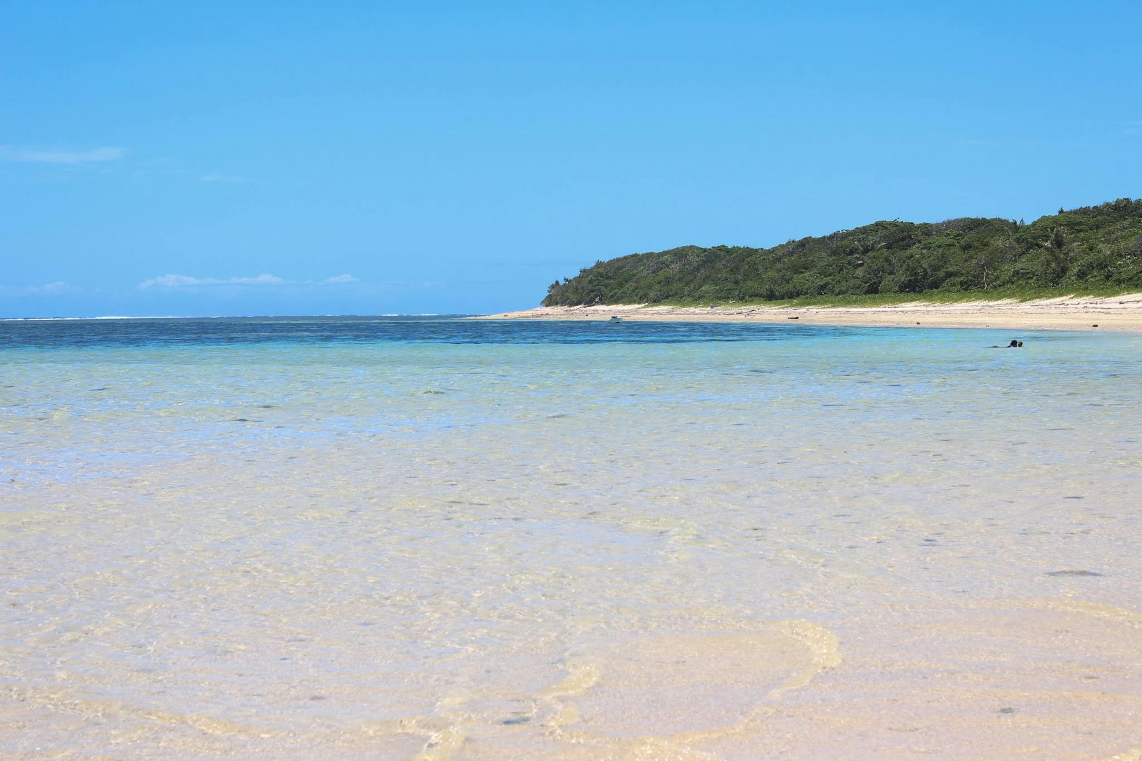 Landschaftsansicht eines blauen Meeres und eines weißen Sandstrandes mit üppigen grünen Hügeln im Hintergrund