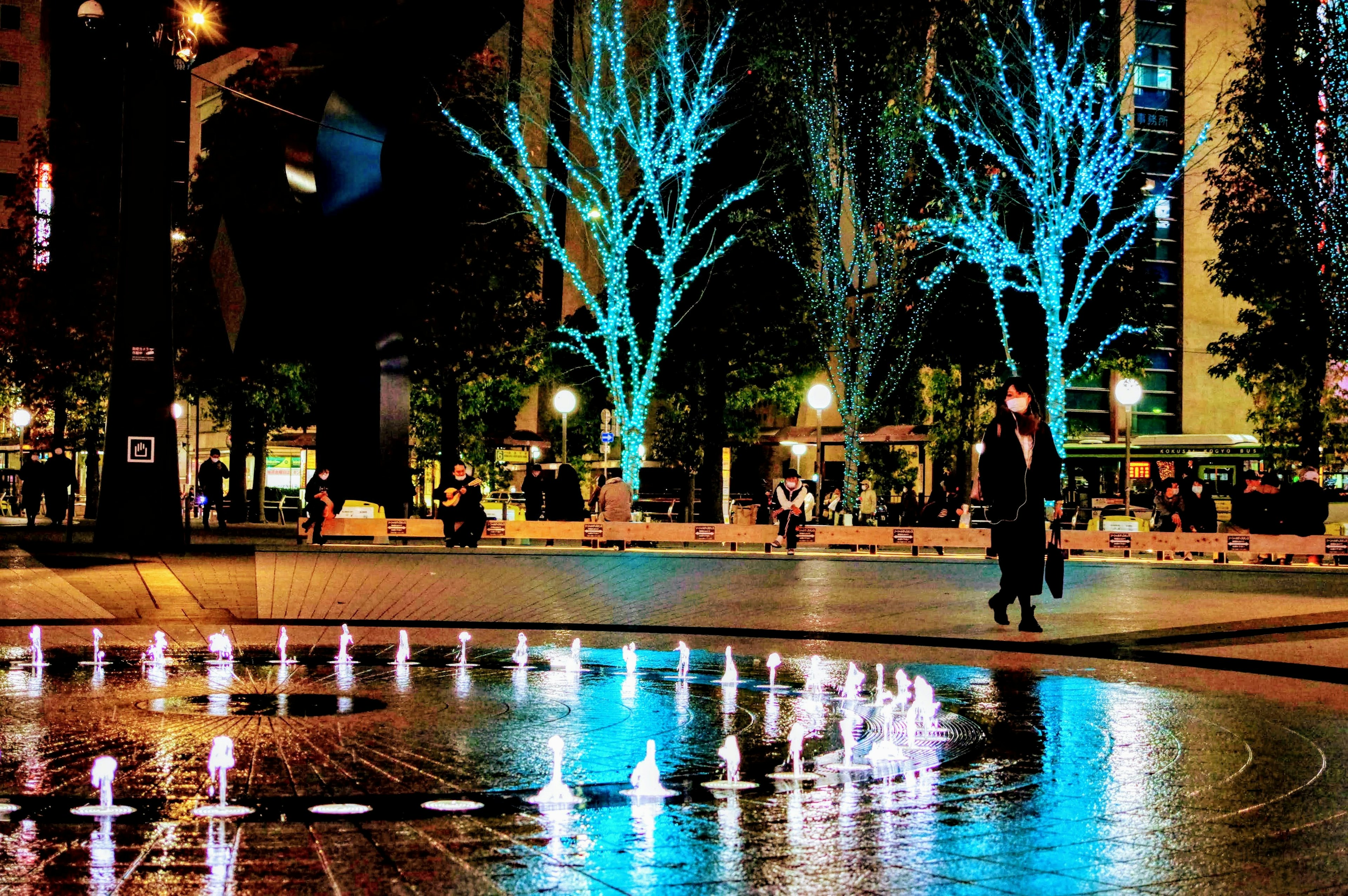 Scène nocturne d'un parc avec des arbres illuminés en bleu et une fontaine