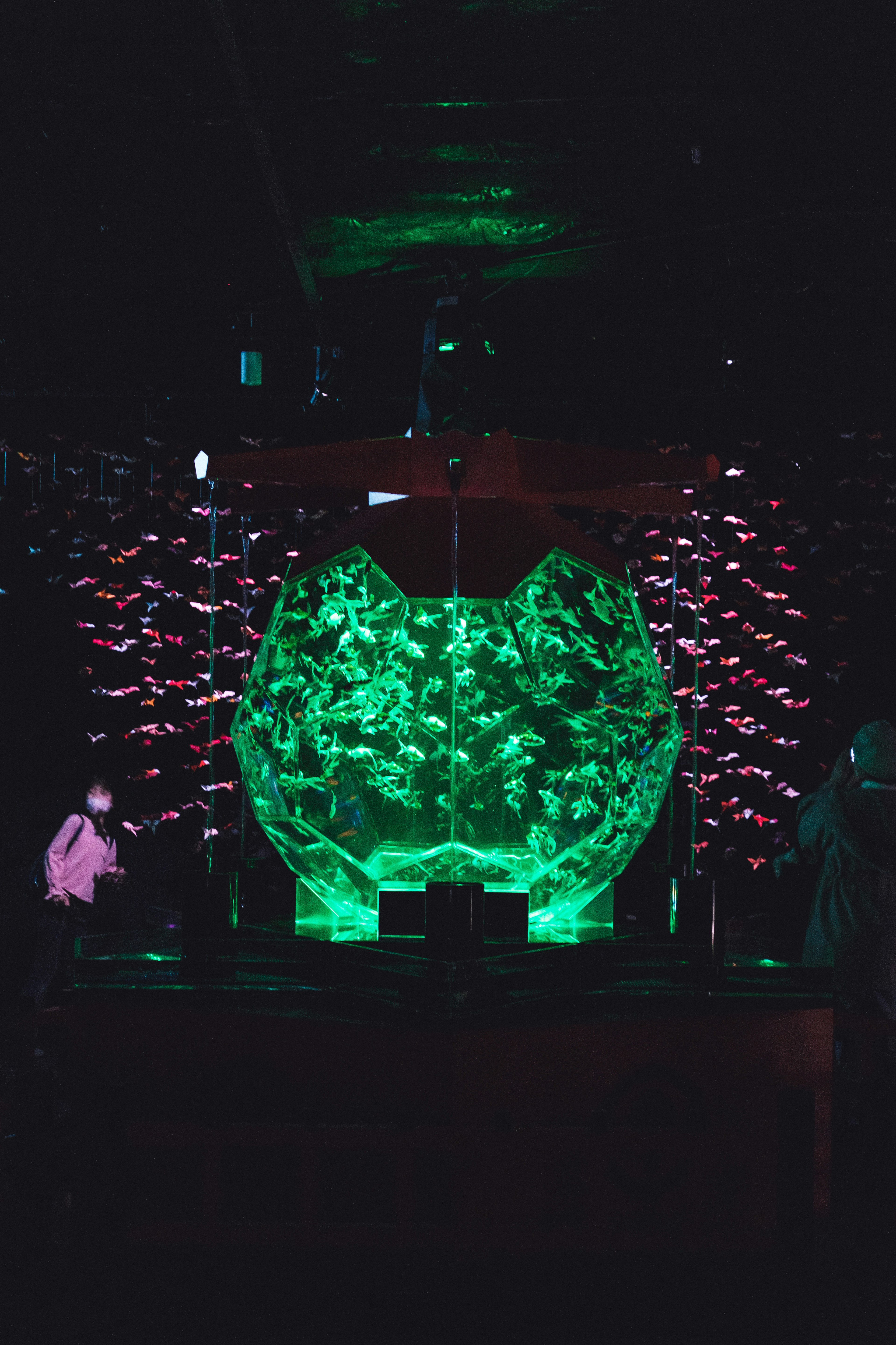 A large crystal object emitting green light surrounded by pink light decorations against a dark background