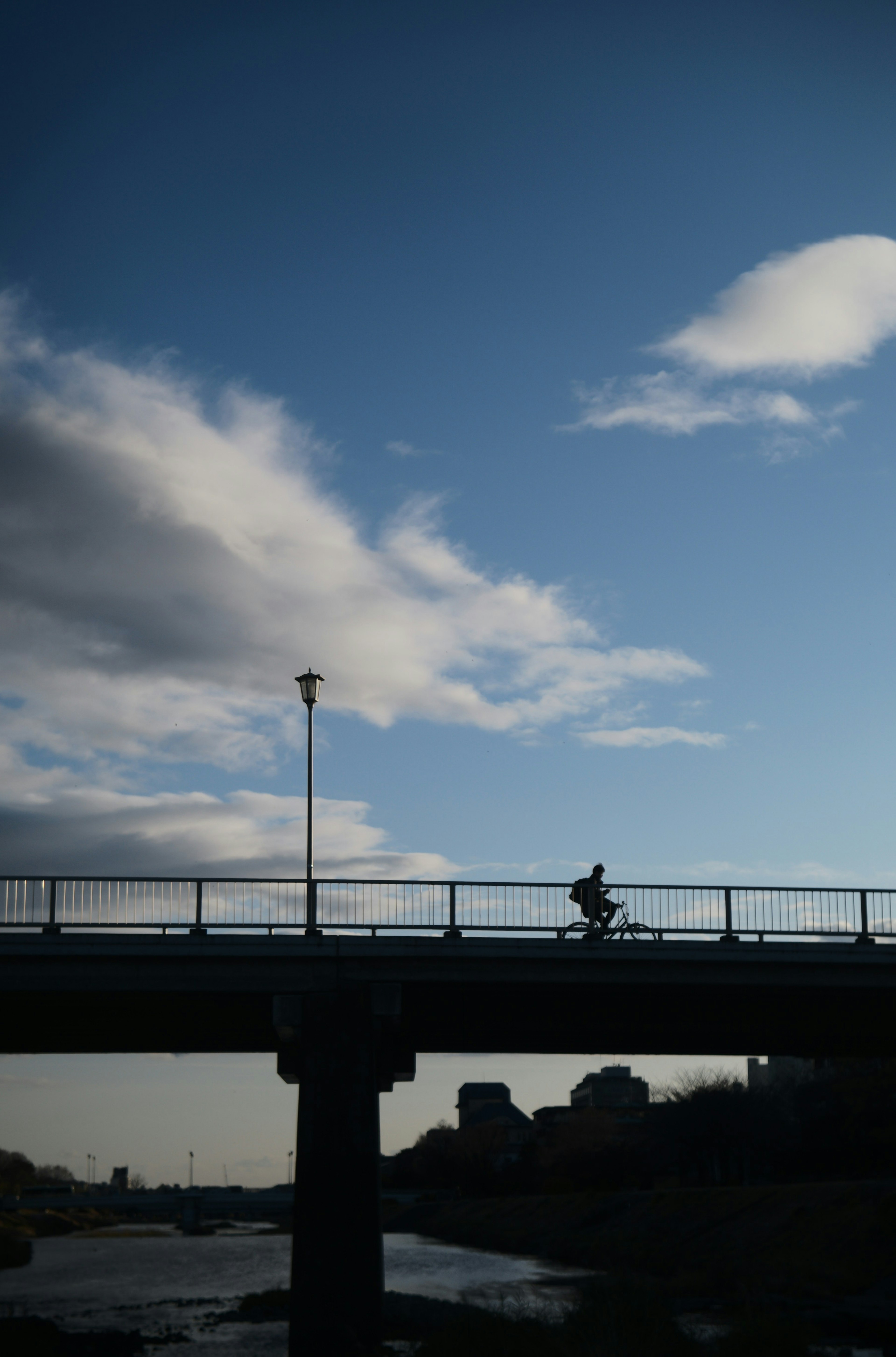 Silueta de una persona montando una bicicleta en un puente bajo un cielo azul