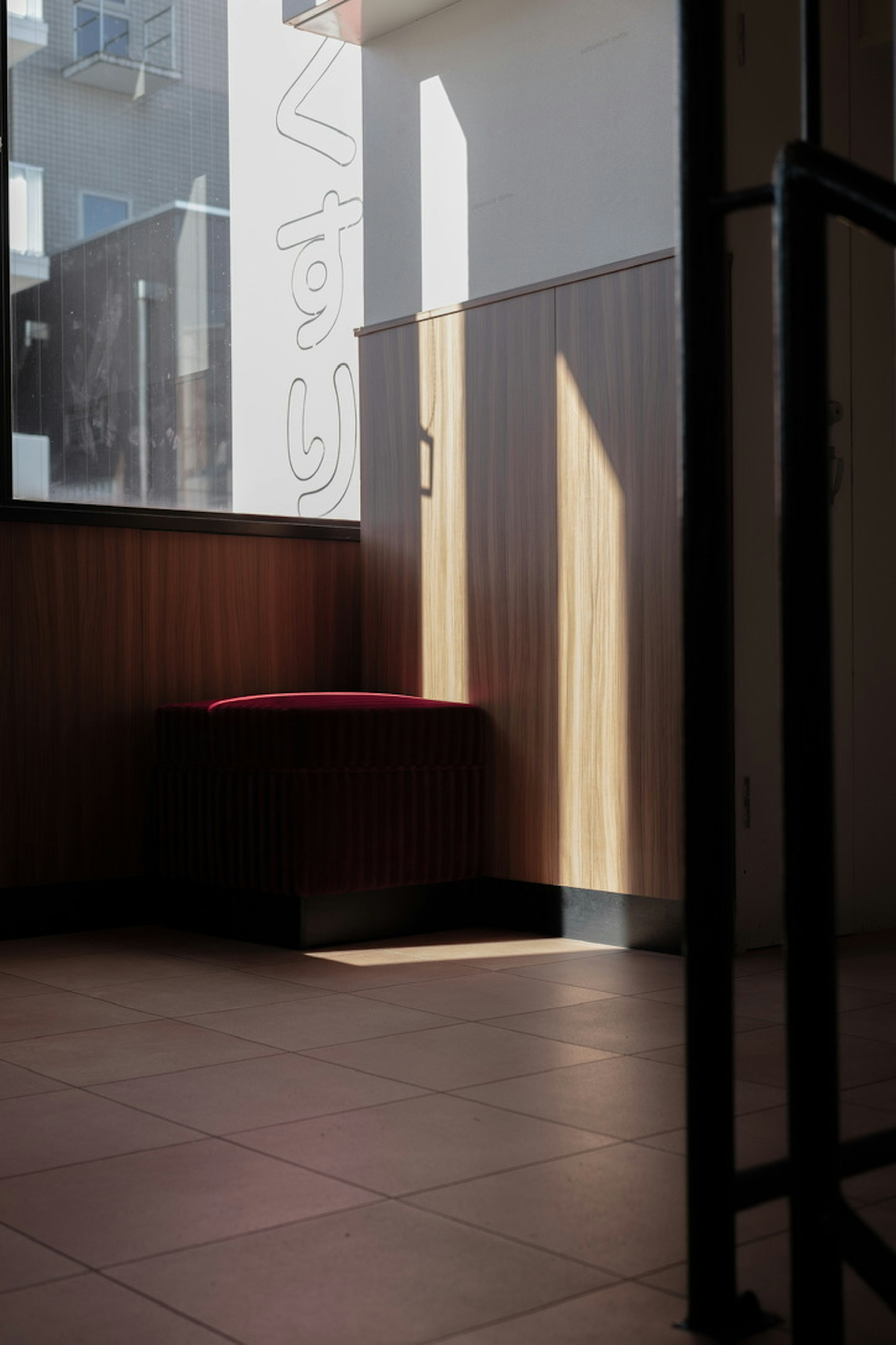 Una esquina luminosa de una habitación con un banco rojo y pared de madera