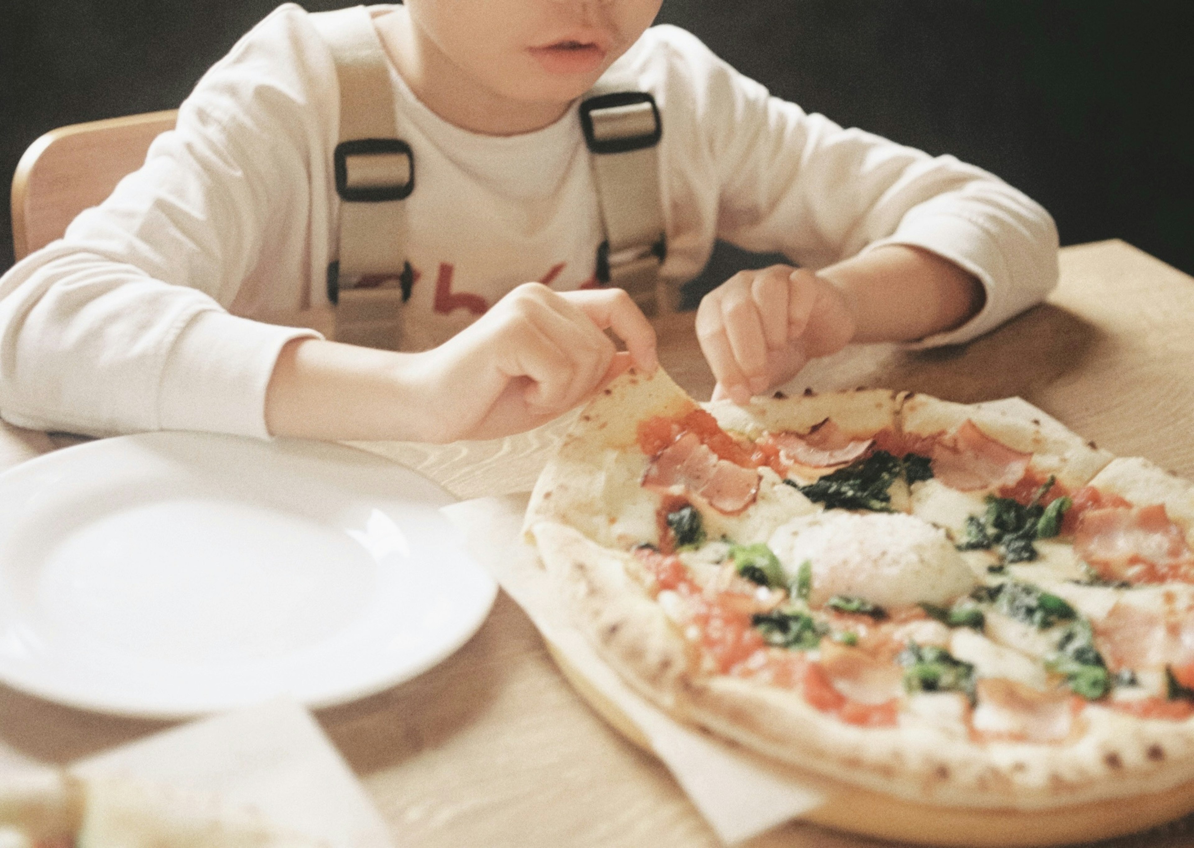 Kind genießt Pizza mit verschiedenen Belägen, Fokus auf die Hände und die Pizza