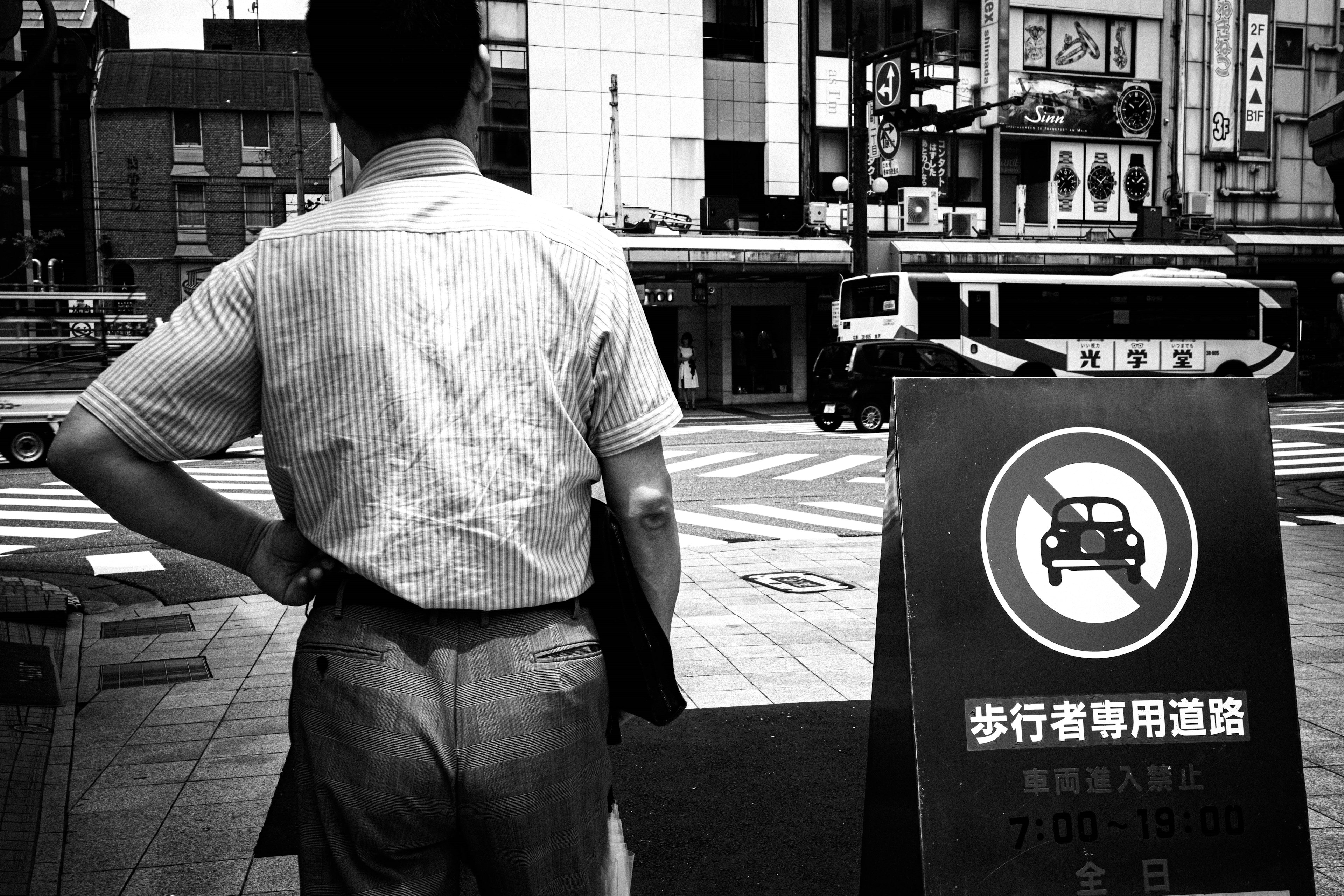 男性が街角で立ち止まり、禁止標識を見つめているモノクロ写真