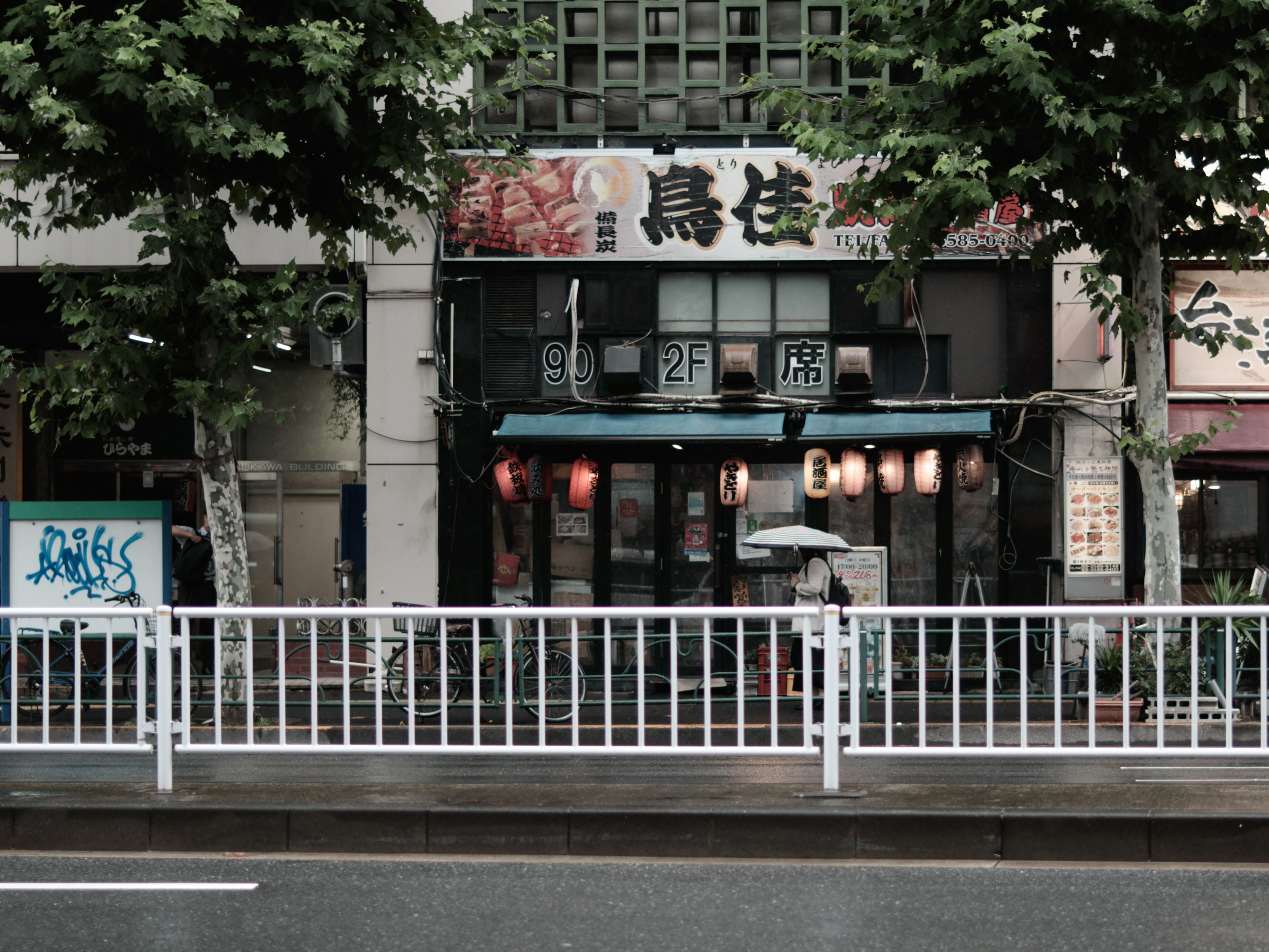 Façade d'une izakaya japonaise traditionnelle dans un cadre urbain avec des fenêtres illuminées et une clôture blanche