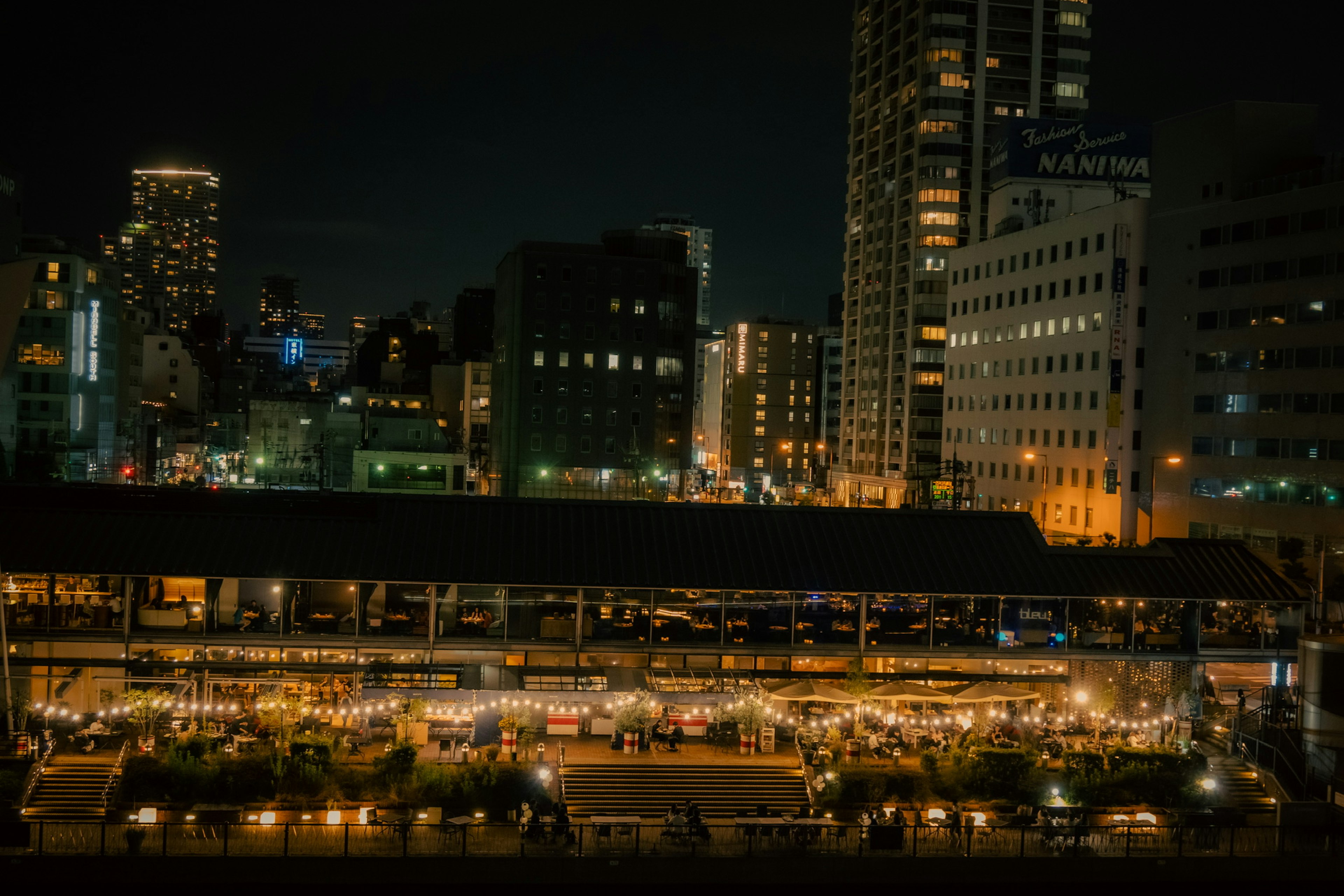 Paysage urbain nocturne avec un marché animé éclairé par des lumières et des gratte-ciel en arrière-plan