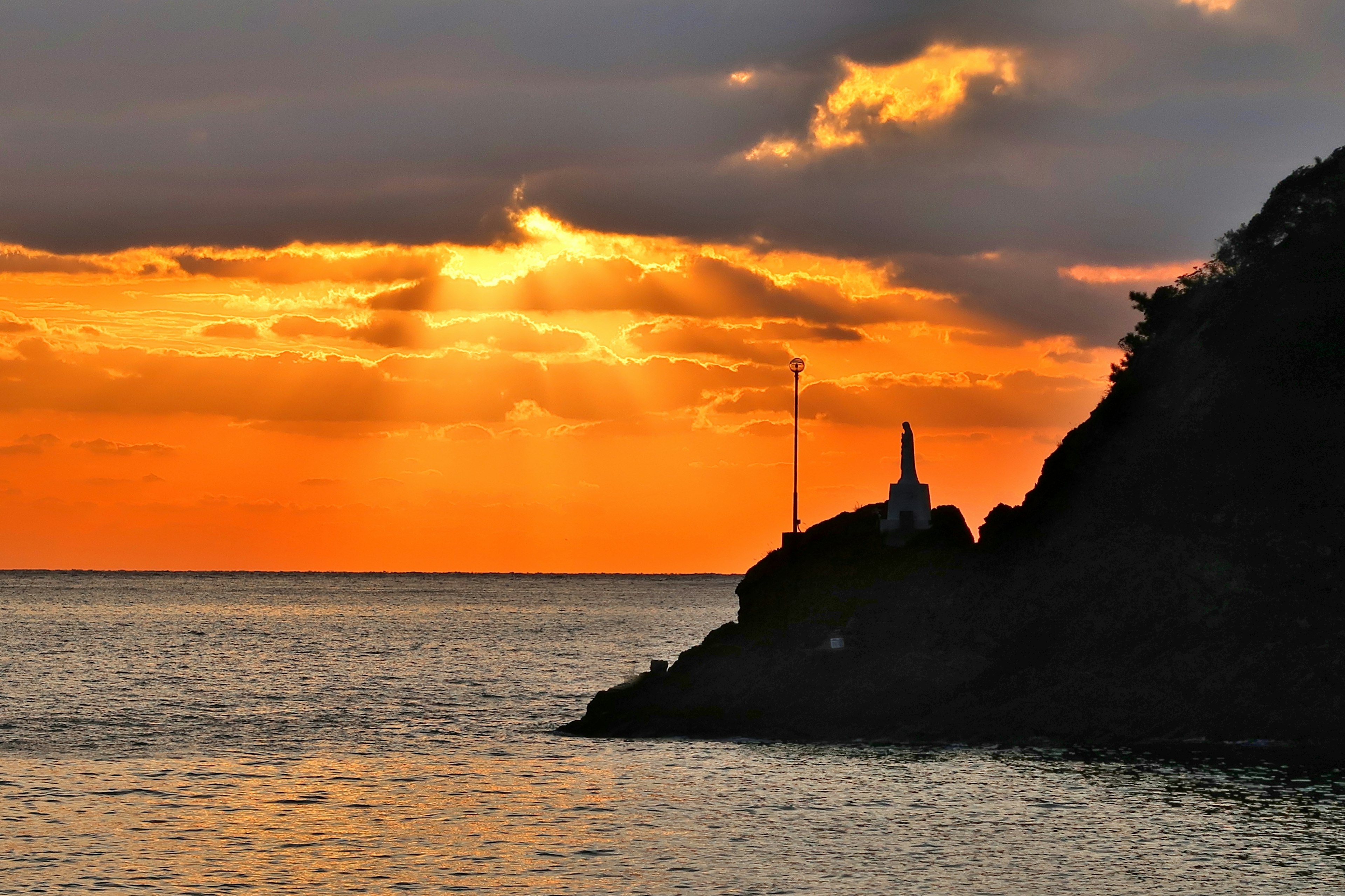 Silhouette einer Küste und eines Berges während eines lebhaften Sonnenuntergangs