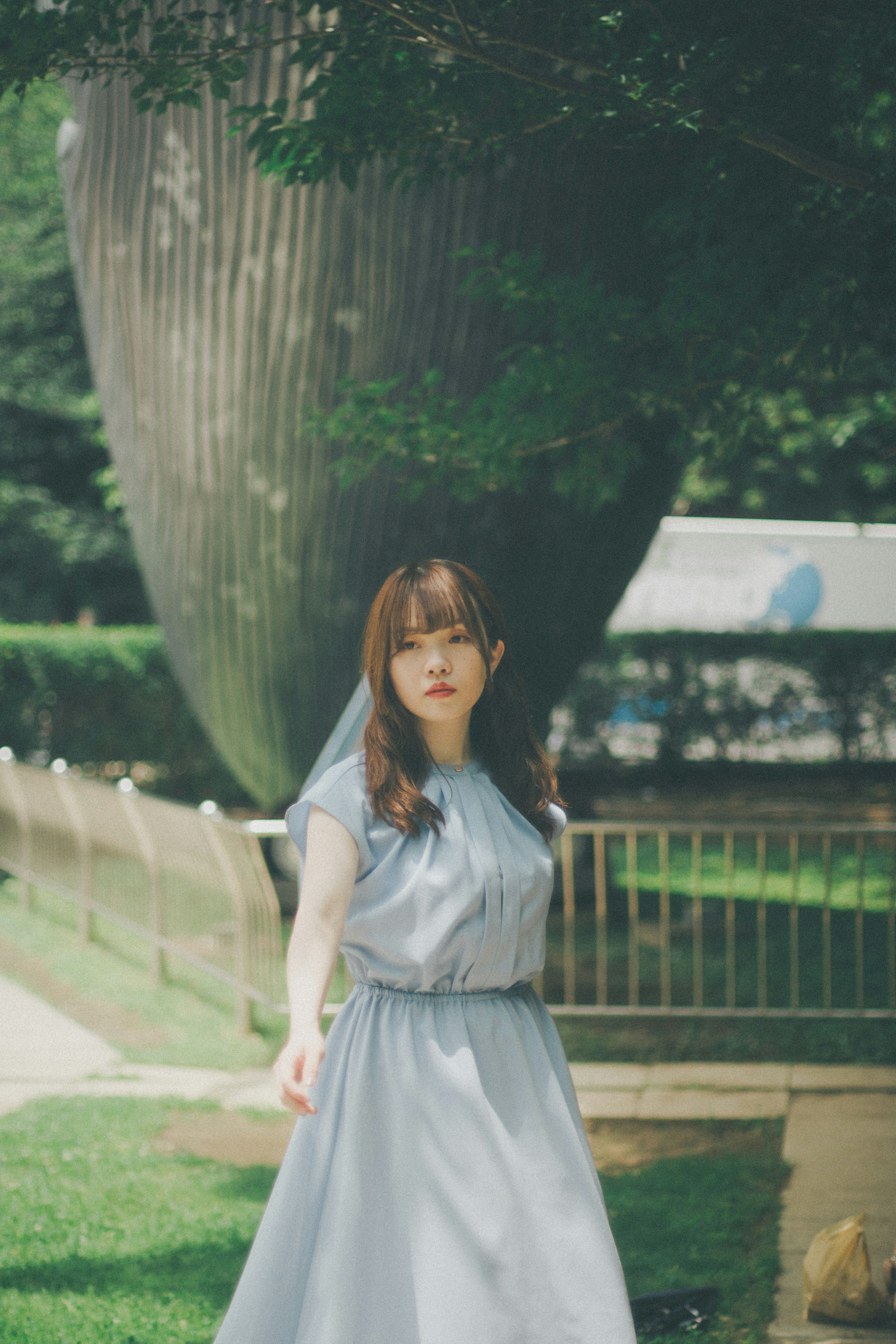 Una mujer con un vestido azul claro de pie en un parque con una gran escultura de fondo