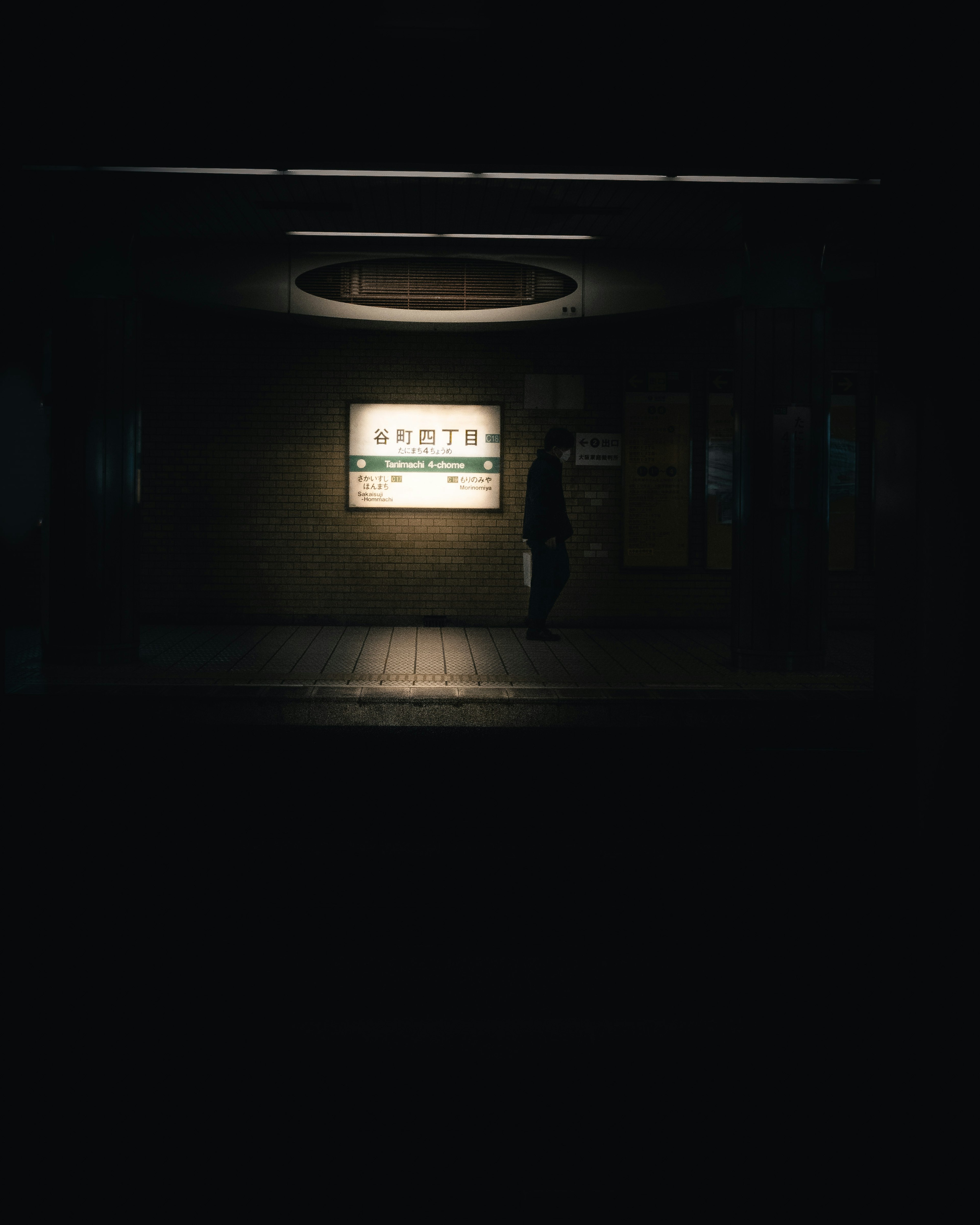 Person standing in a dark corridor illuminated by a glowing sign