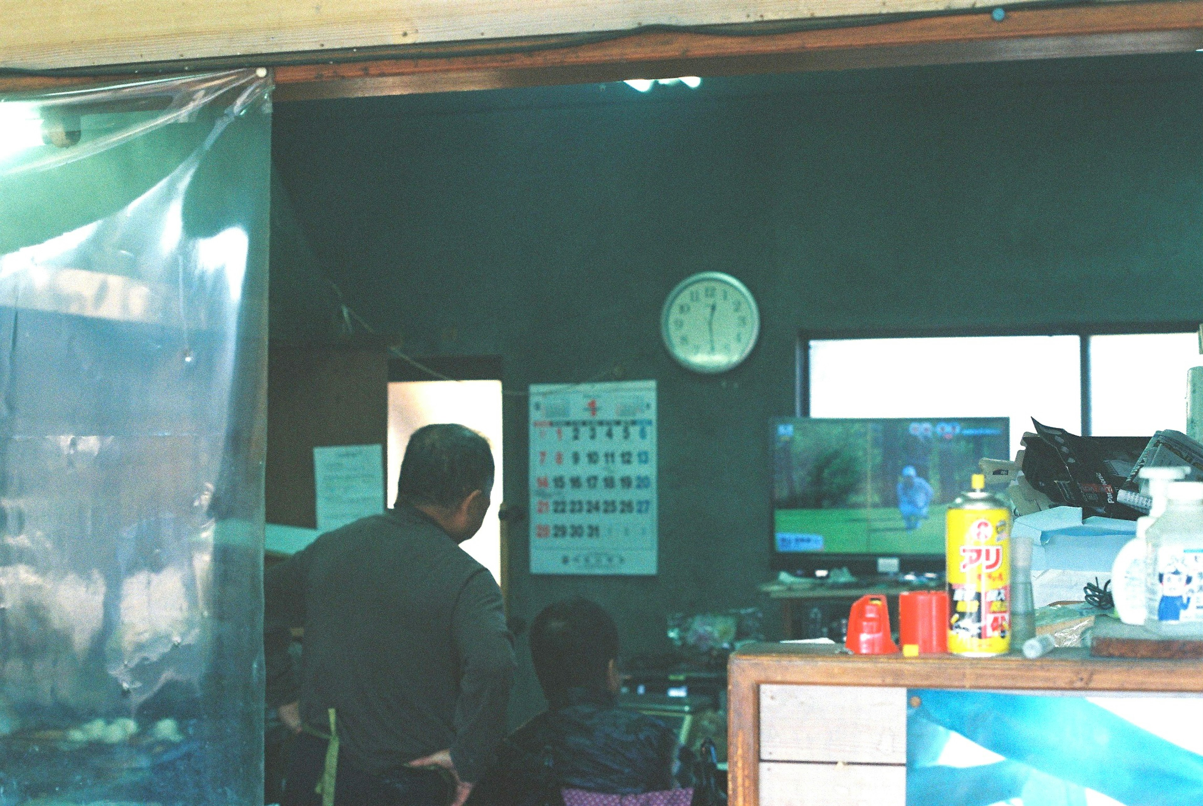 Interior débilmente iluminado con dos personas viendo televisión y un reloj en la pared