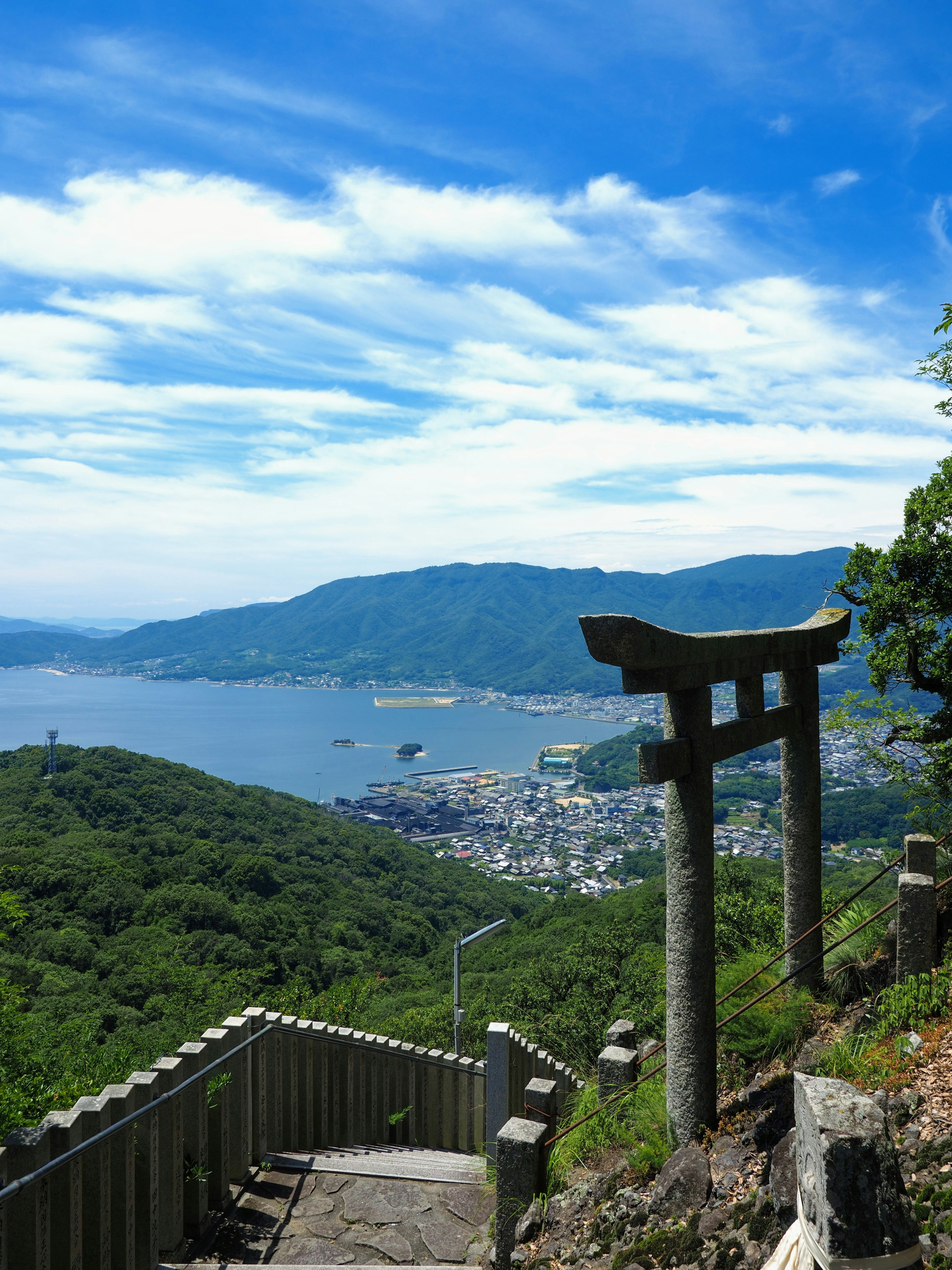 Gerbang torii dengan pemandangan kota dan pegunungan di bawah langit biru