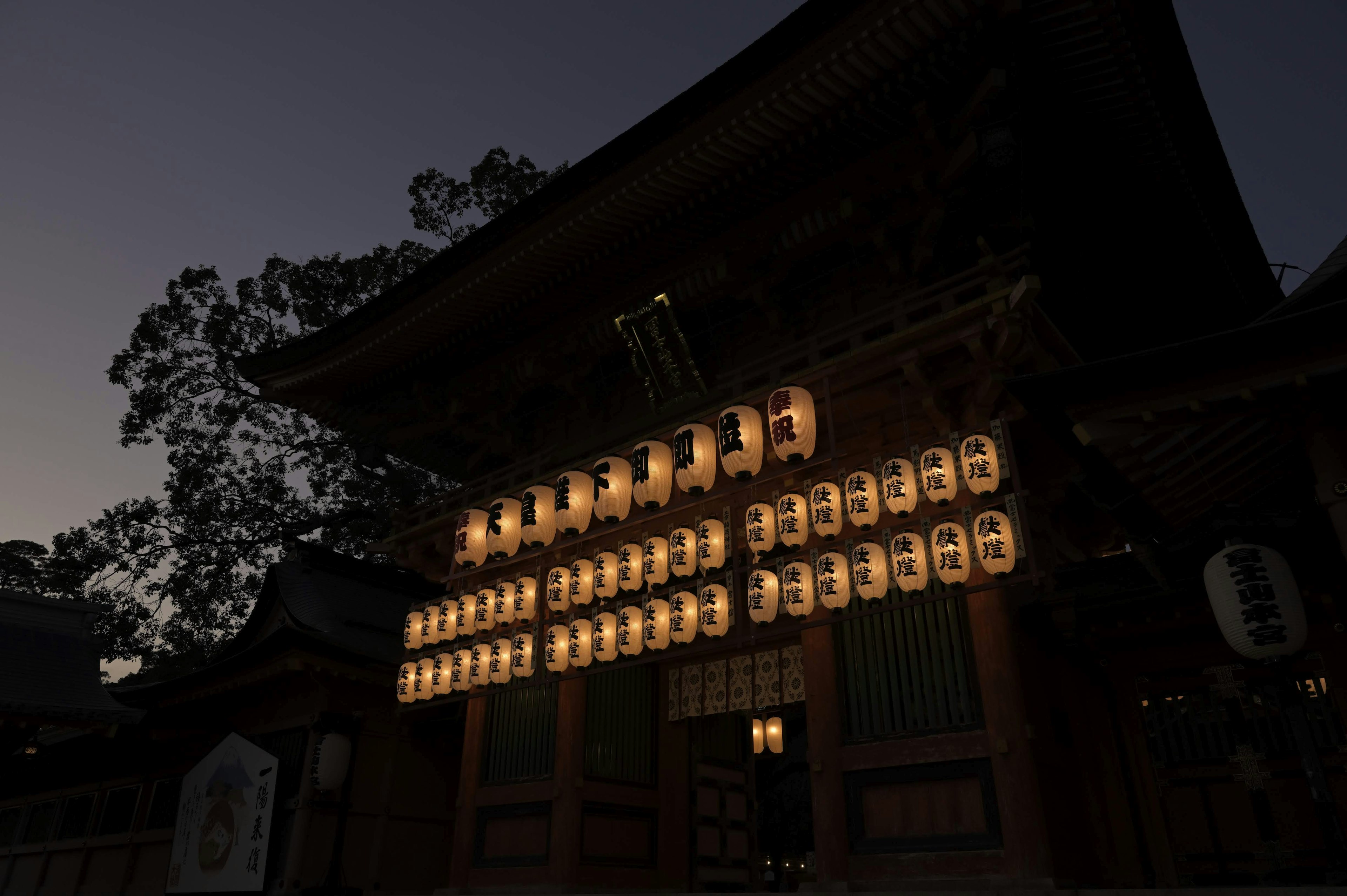 Exterior of a shrine illuminated by lanterns during twilight