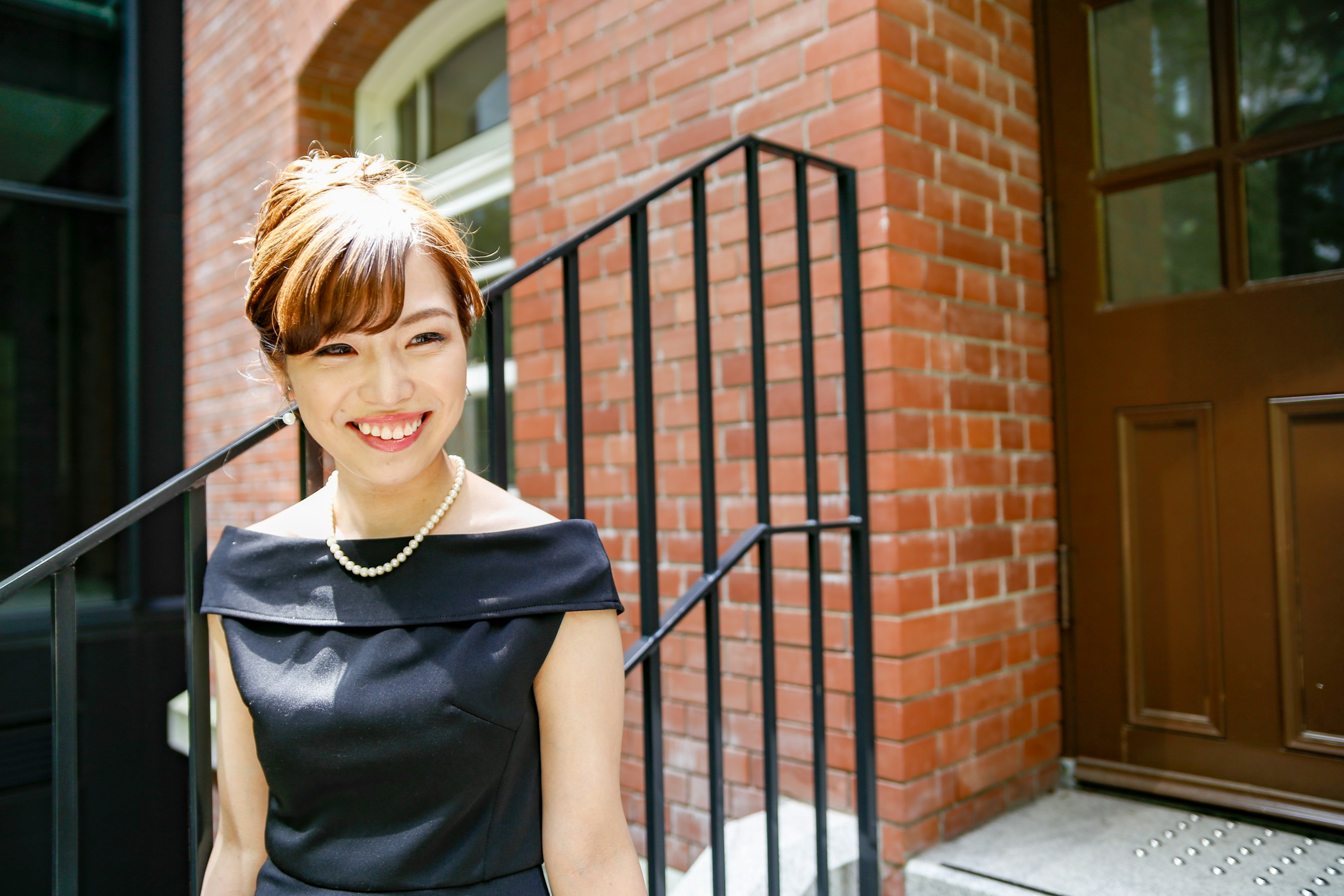 Smiling woman in a black dress standing in front of a brick building