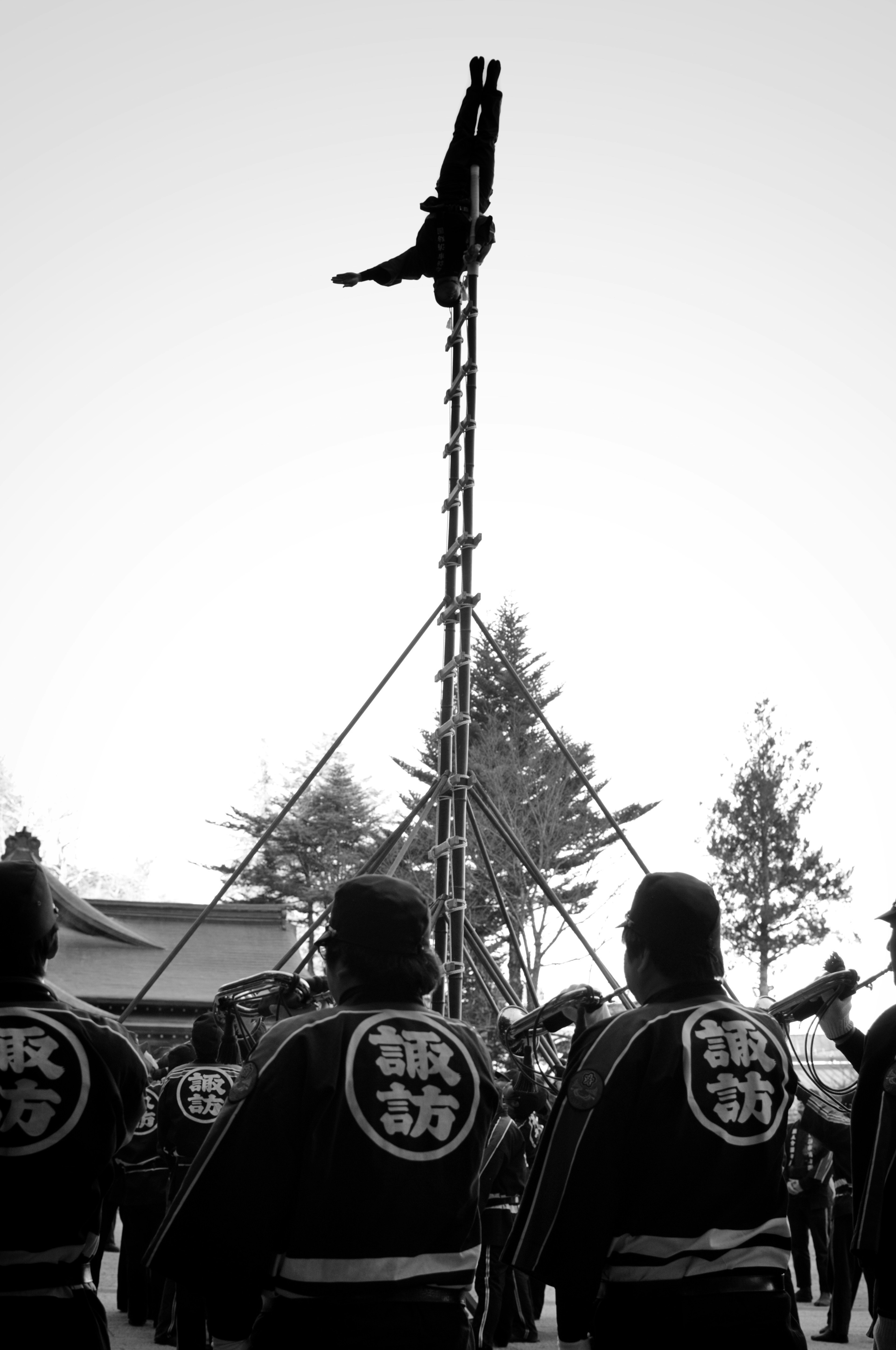 黒白の祭りのシーンで高い梯子の上に立つ人とその周りの参加者