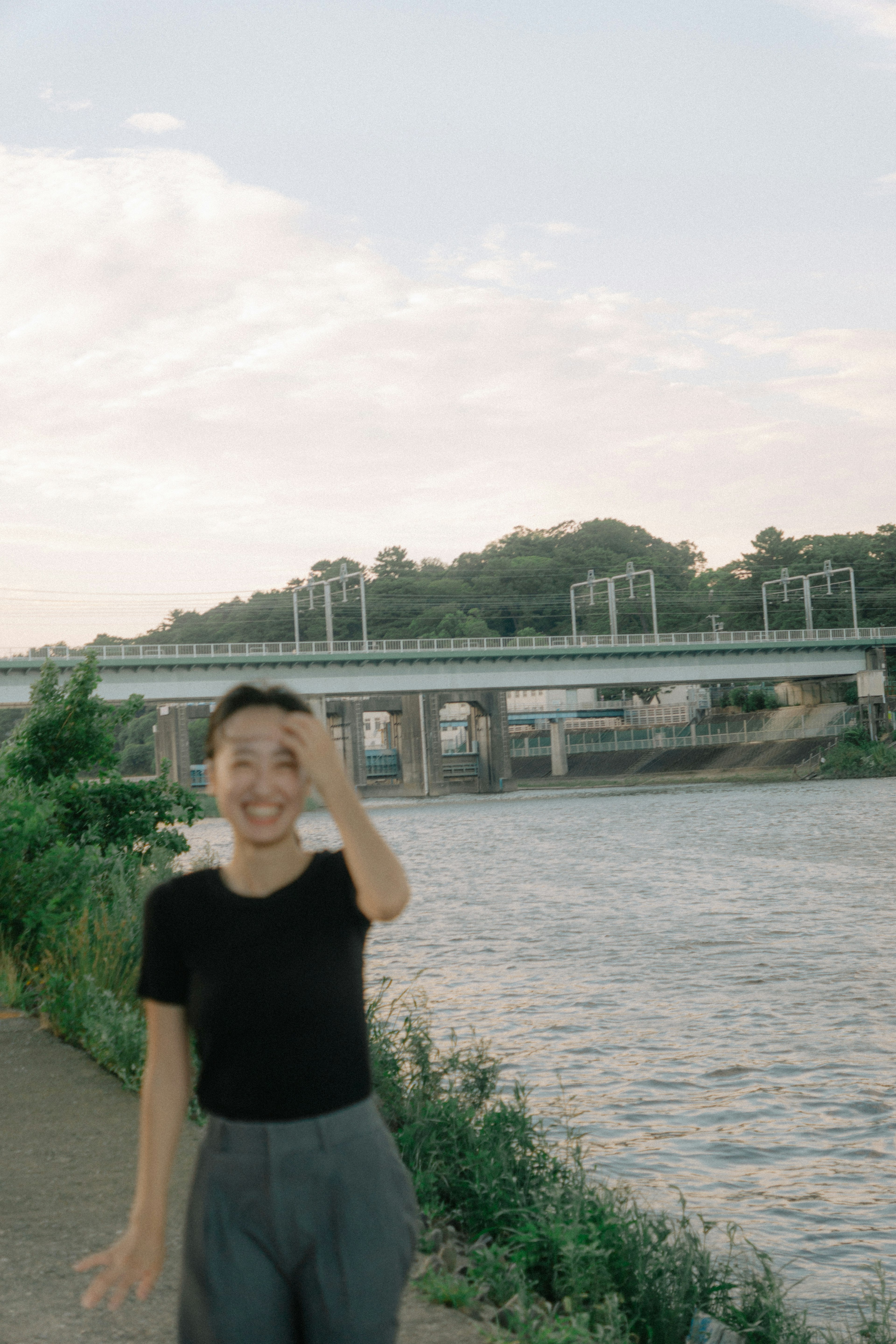 Una mujer sonriente de pie junto al río con un puente al fondo