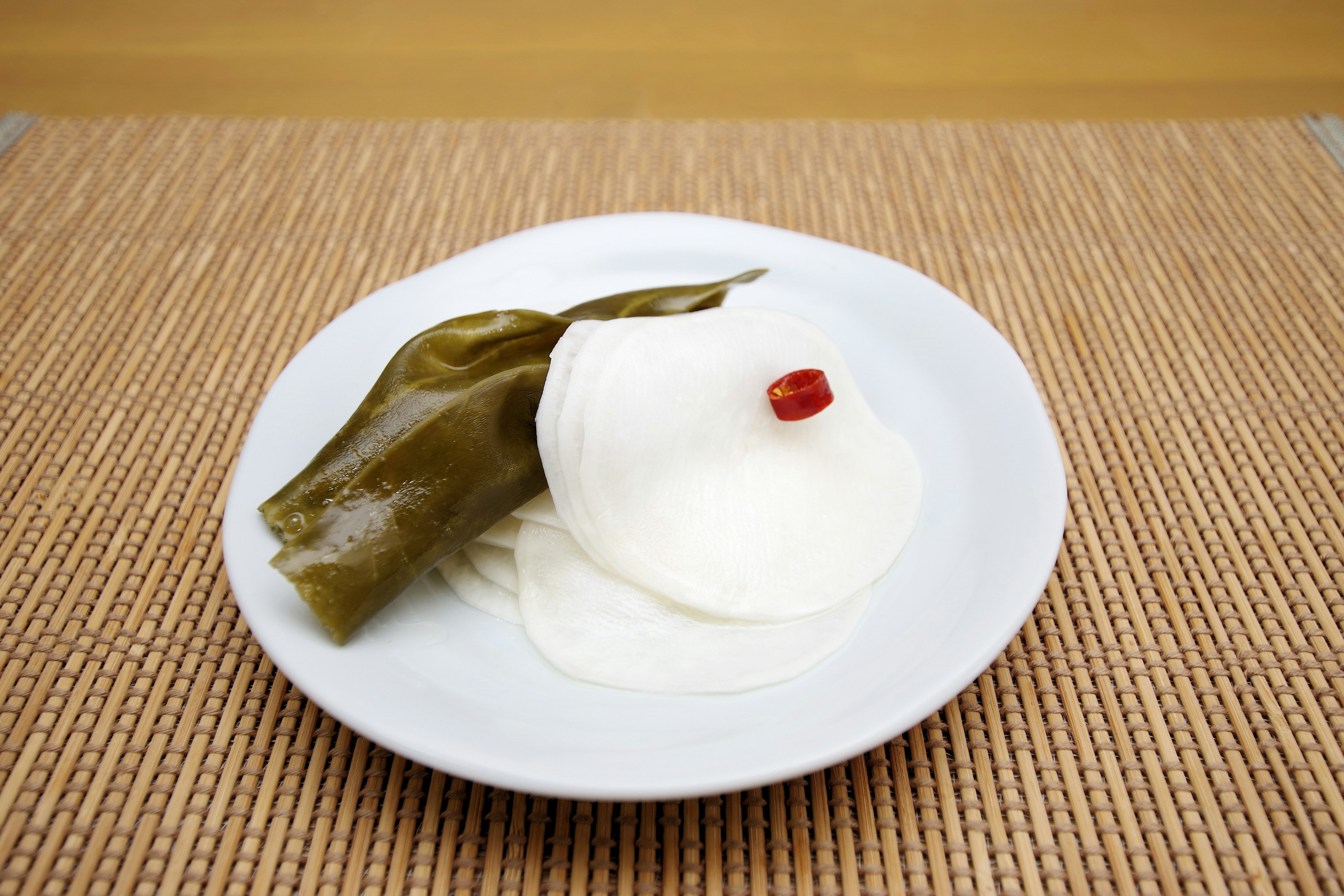 Rodajas de rábanos daikon y un trozo de alga en un plato blanco con una baya roja